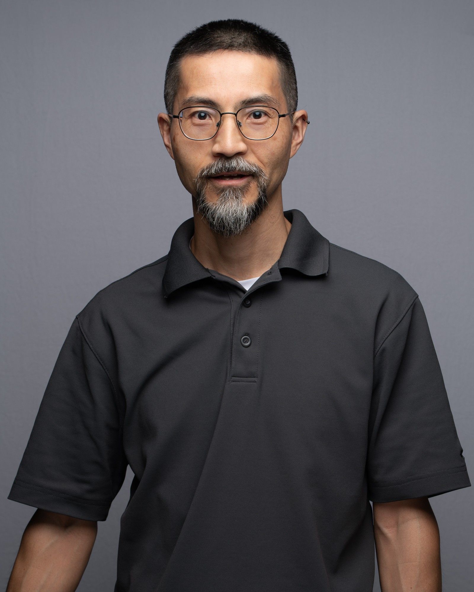 a portrait of a middle-aged Japanese man wearing a gray short-sleeve polo shirt.