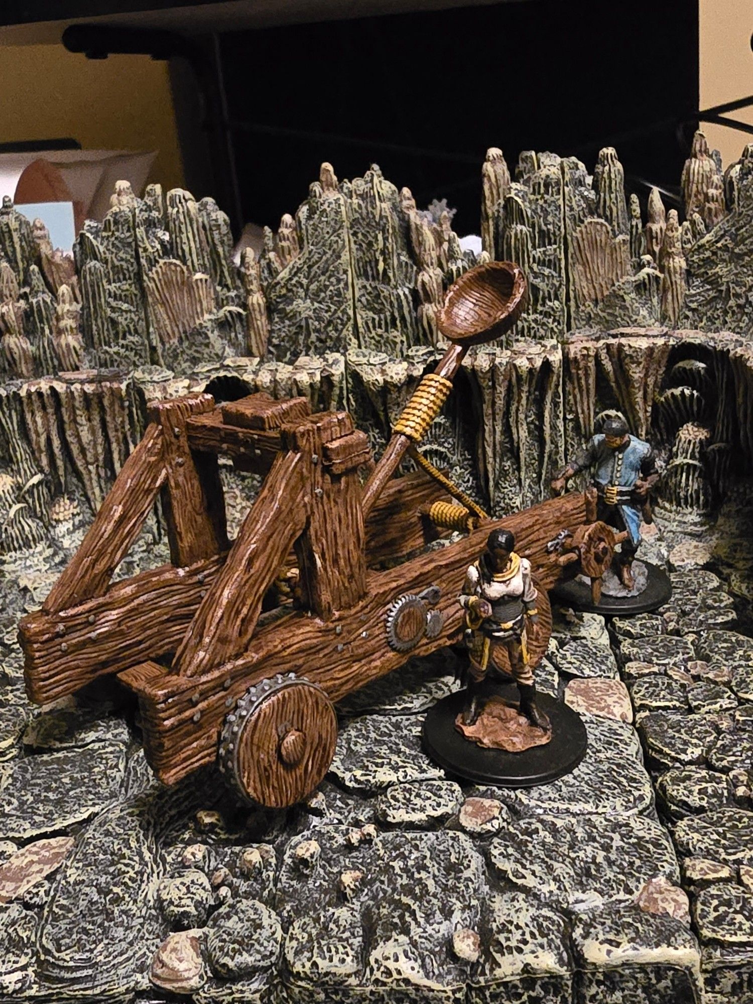 A custom painted catapult miniature, with two human miniatures for scale.