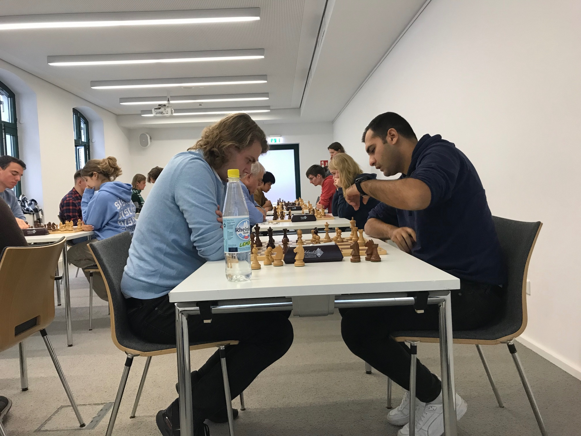 Zwei Studenten spielen Schach. Im Hintergrund laufen weitere Partien.