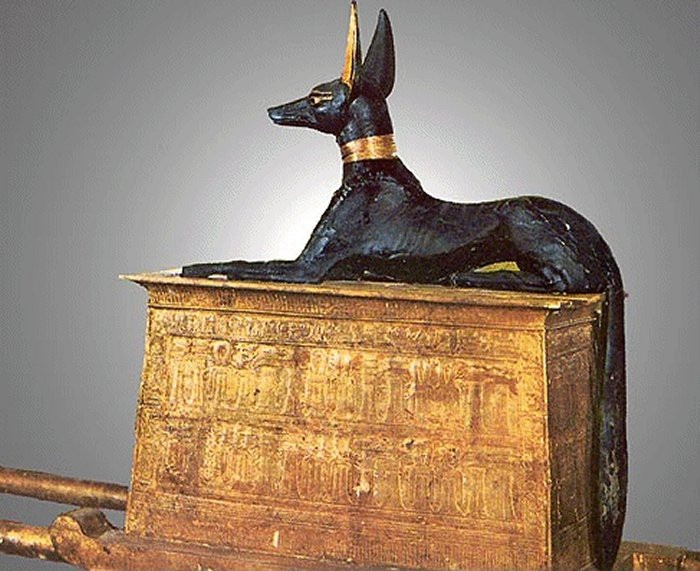 A statue of the Egyptian god Anubis, reclining on a golden chest.