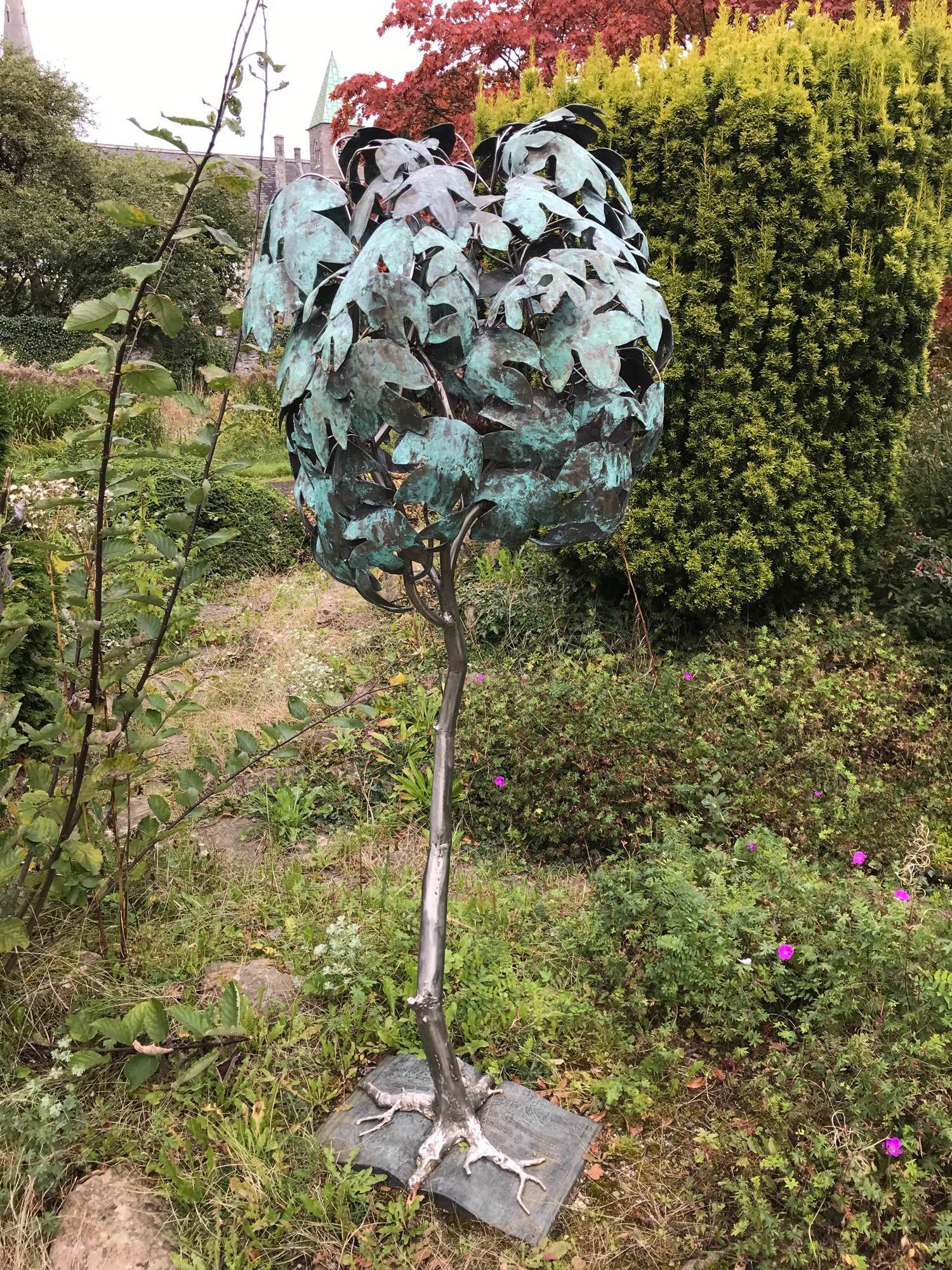 Metallic statue of a young leafy tree in the middle of a garden