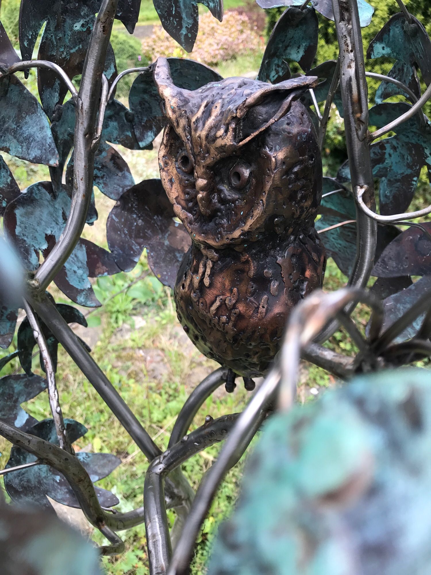 Small metallic statue of an owl in the middle of the crown of a metallic statue of a tree