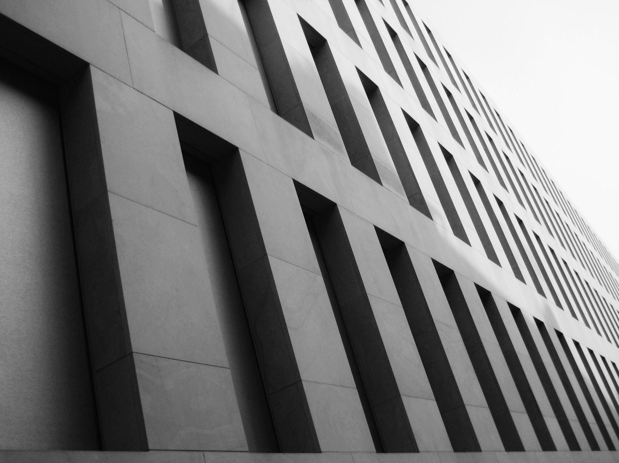 Schwarz-Weiß-Foto der Diöszesanbibliothek in Münster, NRW. Die zahlreichen rechteckigen, parallel angeordneten Fenster scheinen aufgrund der Perspektive nach hinten zu stürzen.