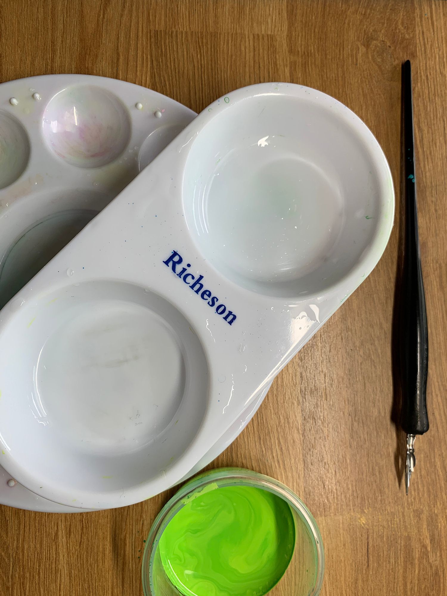 Photo of a clean white palette and a two well bowl, a dip pen and a plastic container with brightly colored ink.