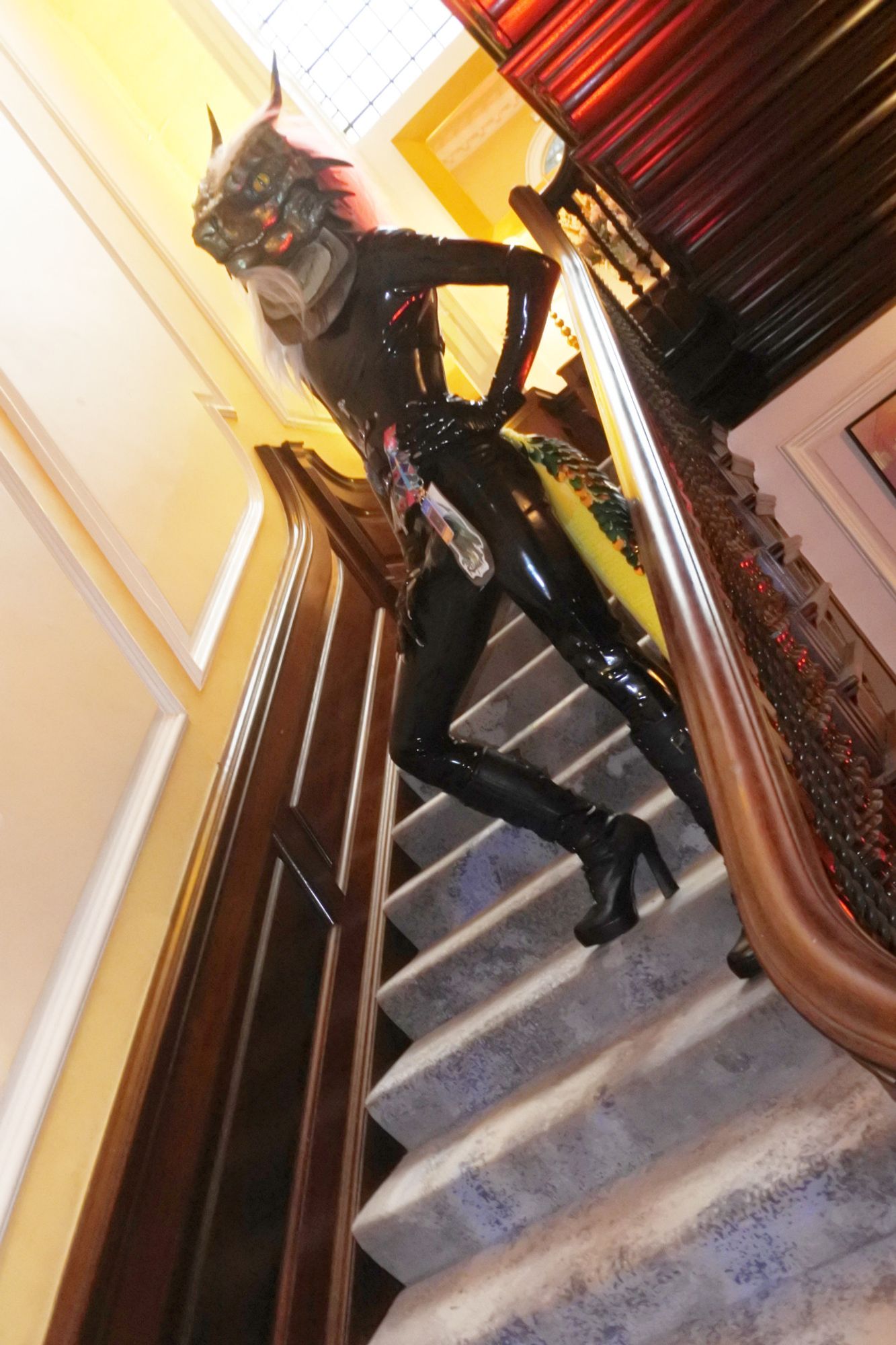 Fursuit photo - Righin the green dragon poses on the main stairwell at Pawsome.  He is wearing a glossy black latex catsuit, claw gloves and high-heeled leather boots.

Photo taken by Mutley