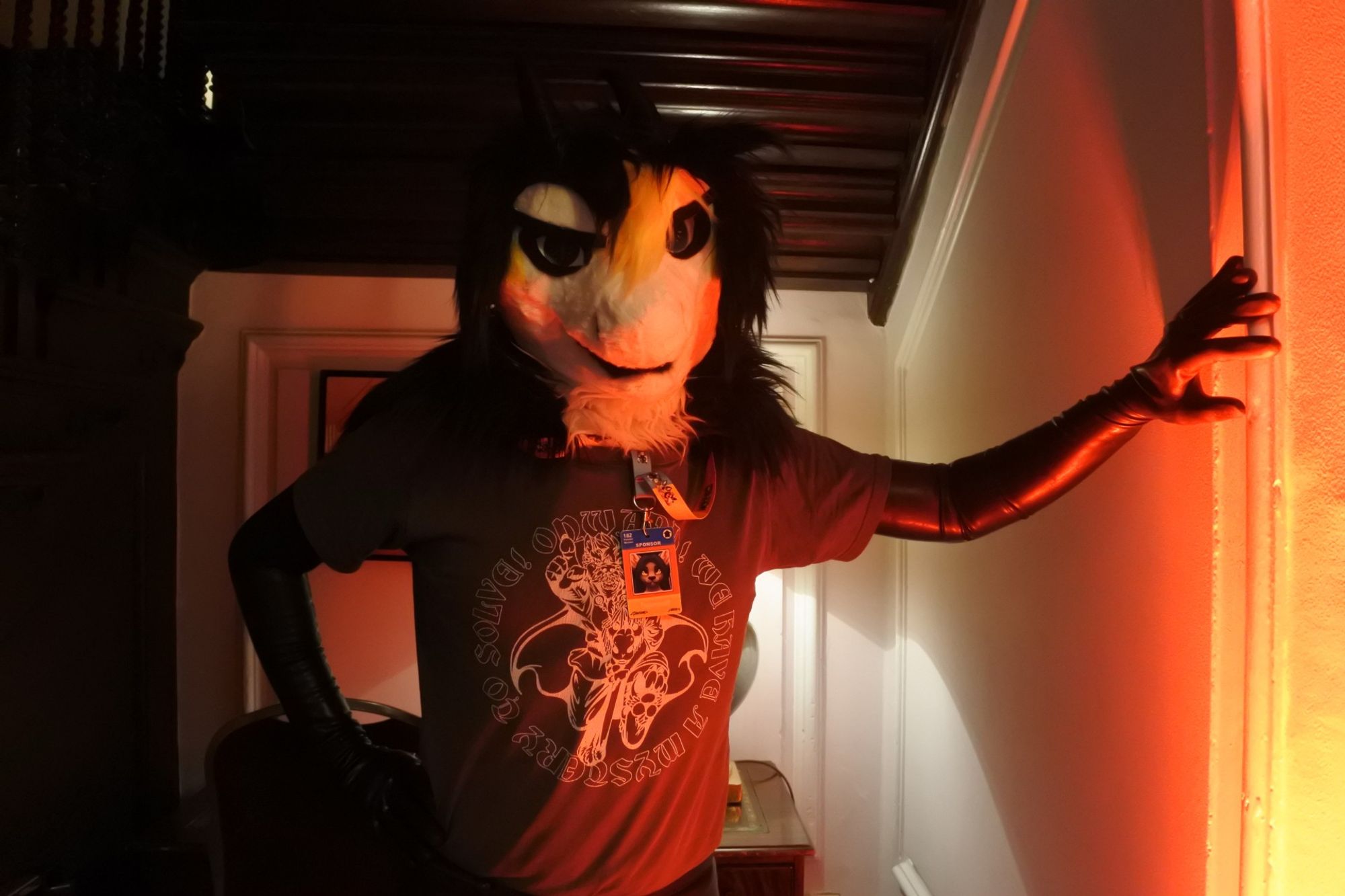 Fursuit photo of a black white and yellow dragon, wearing latex opera gloves.  He's standing next to a red light causing the gloves to reflect a red tint

Photo by Mutley