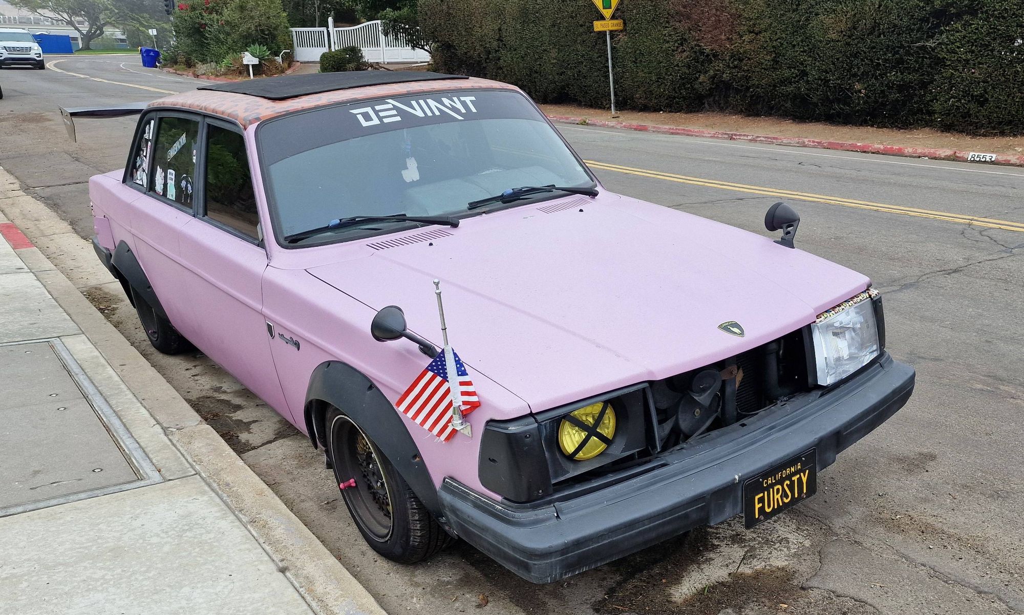 A pink 200 series Volvo, with black bumpers ans wheel arch extensions. It also has various stickers and a big raised rear spoiler.