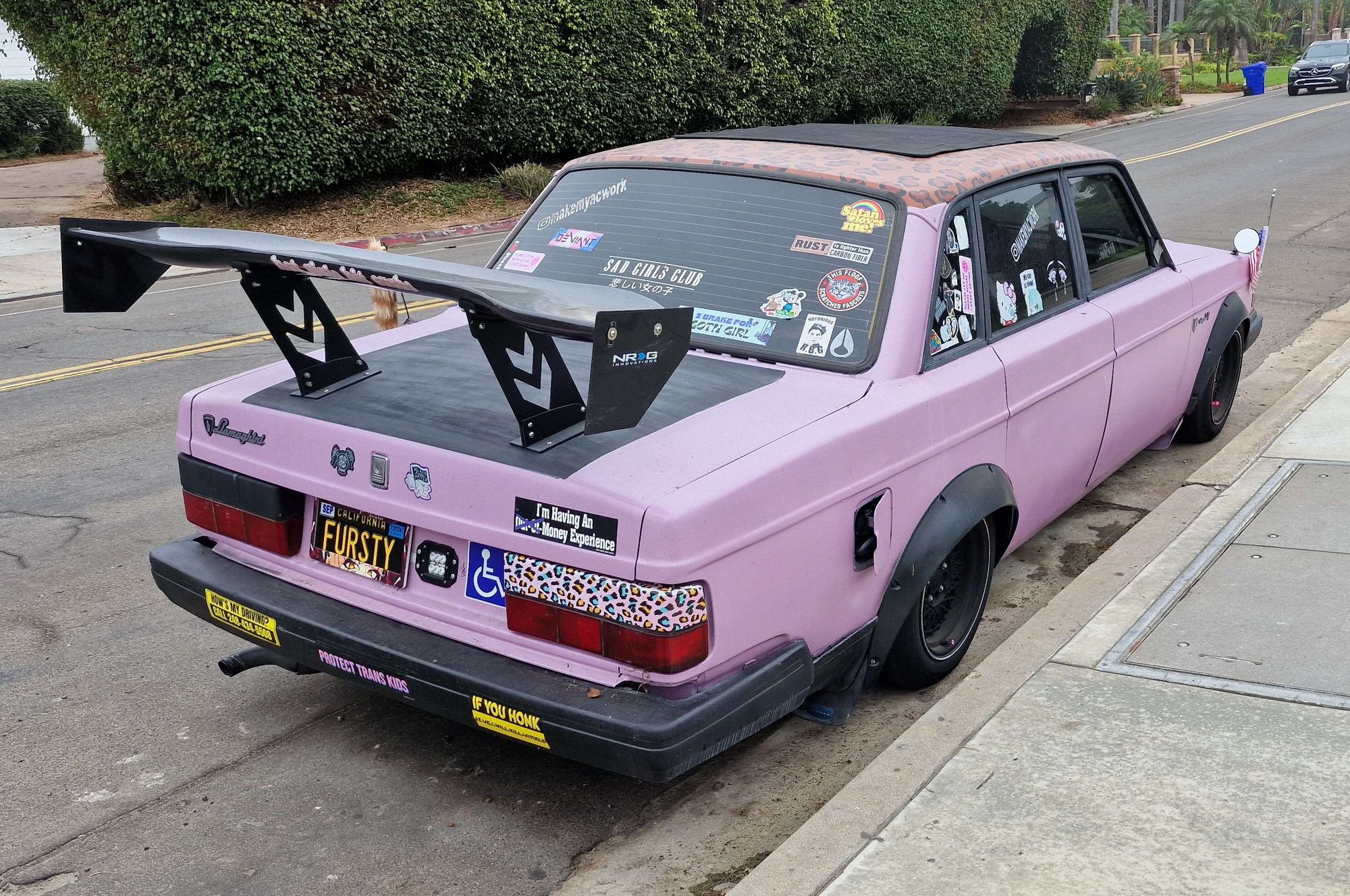 A pink 200 series Volvo, with black bumpers ans wheel arch extensions. It also has various stickers and a big raised rear spoiler.