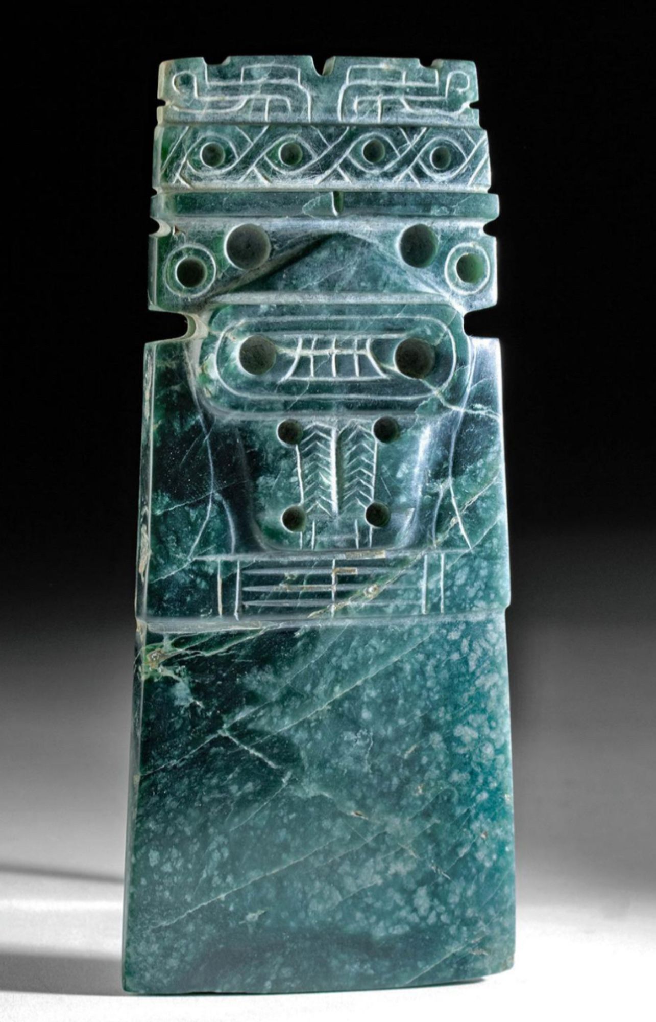 Dark green, pre-Colombian jade celt carved with an image of a person with clasped hands hands , possibly a shaman. Image from invaluable.com.