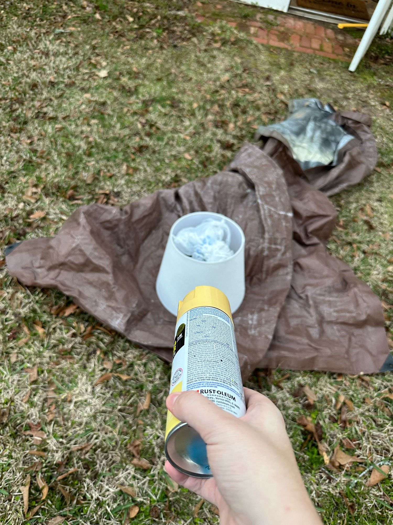 white lampshade with a brown tarn under it and me pointing a can of yellow spray paint at it