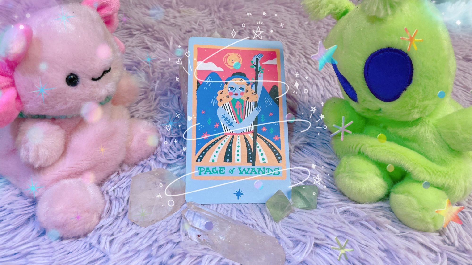 momo the axolotl and schmeebo the alien - both pudgy lil plushies - bookend the page of wands tarot card from the rainbow tarot. several clear quartz and fluorite lay in front of the card. the image has been edited to add sparkles and flourish.