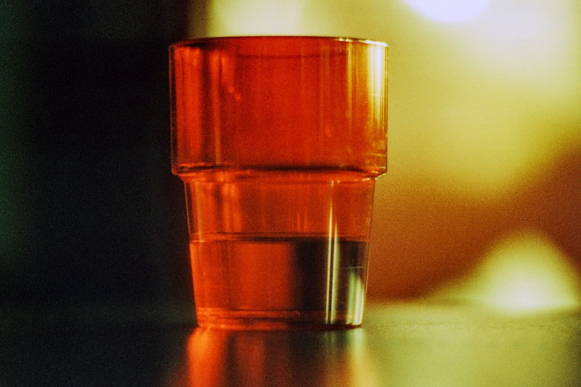 A backlit red plastic glass on a reflective surface. Blurry background.