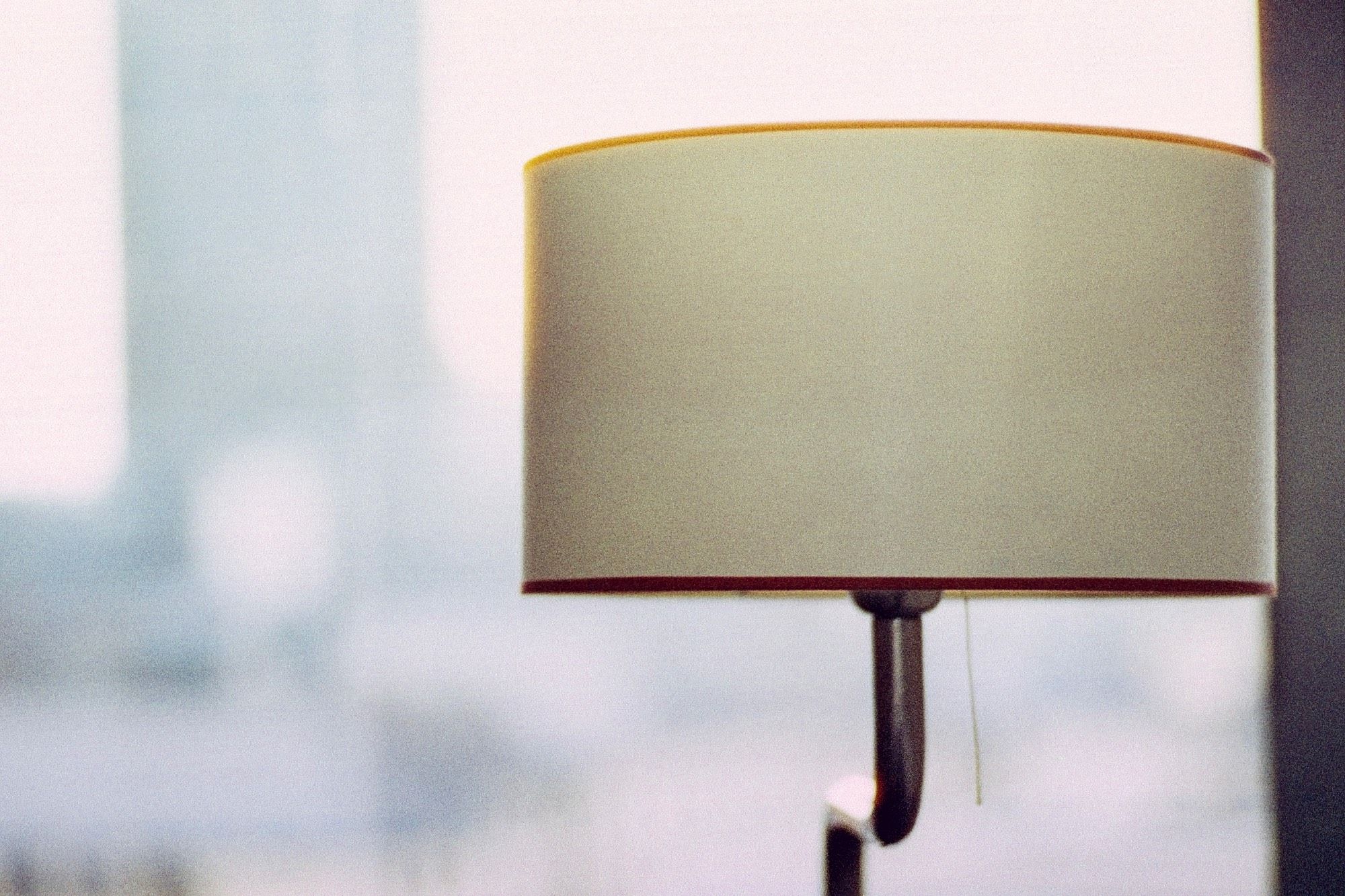 A lamp with a lampshade in front of a window. Blurry background.