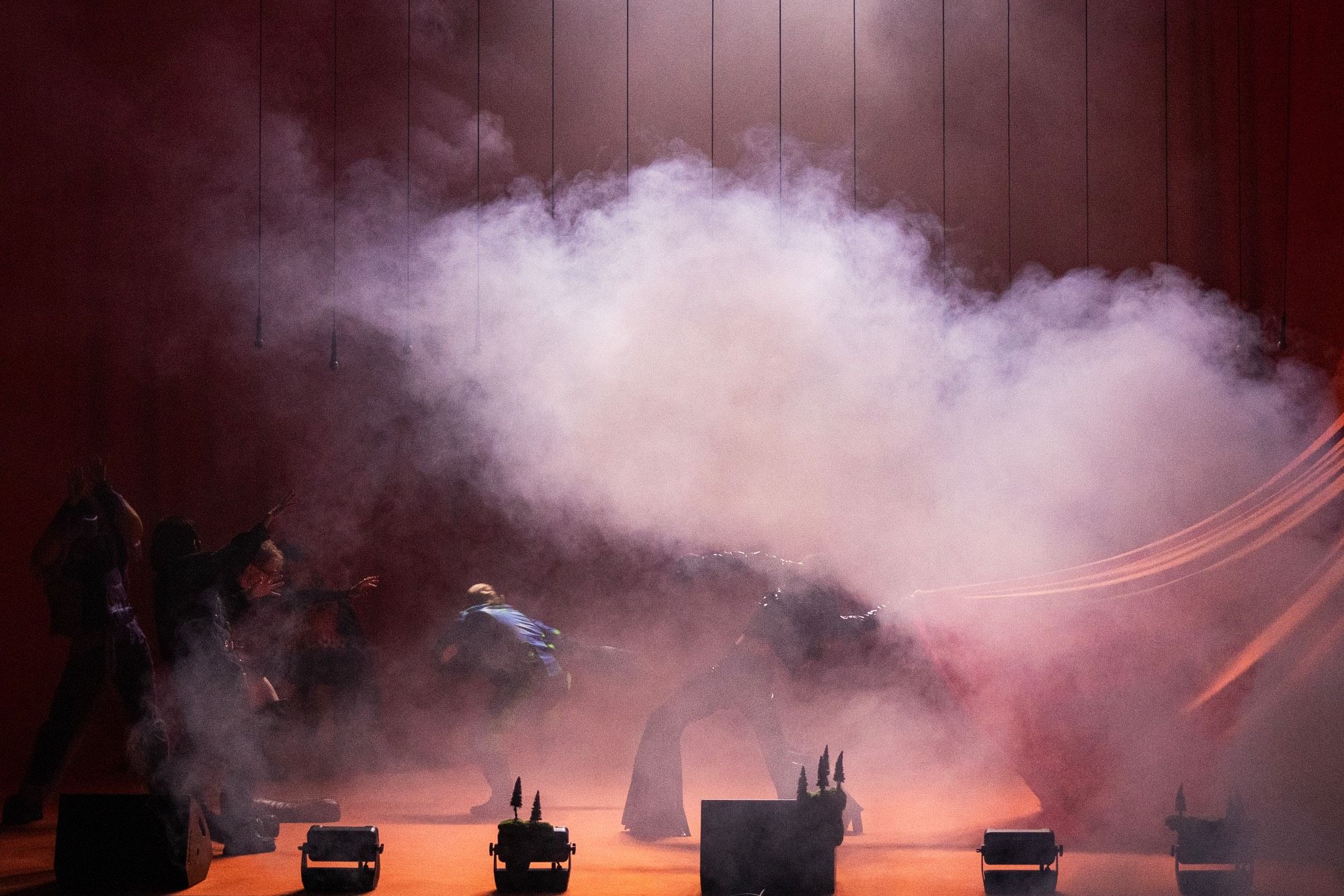 Dancers performing on stage with a lot of smoke in from of an orange backdrop.