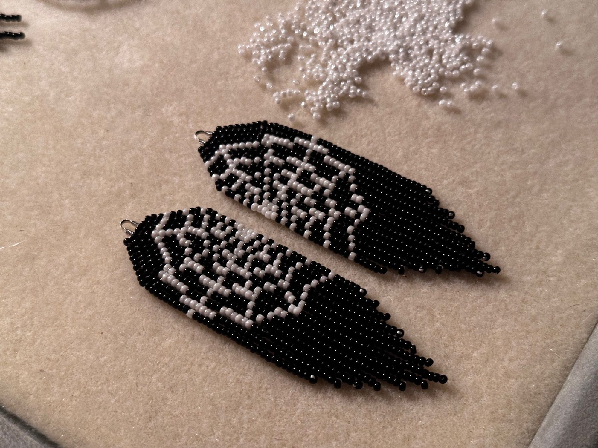 A pair of black and white cobweb earrings on a bead mat