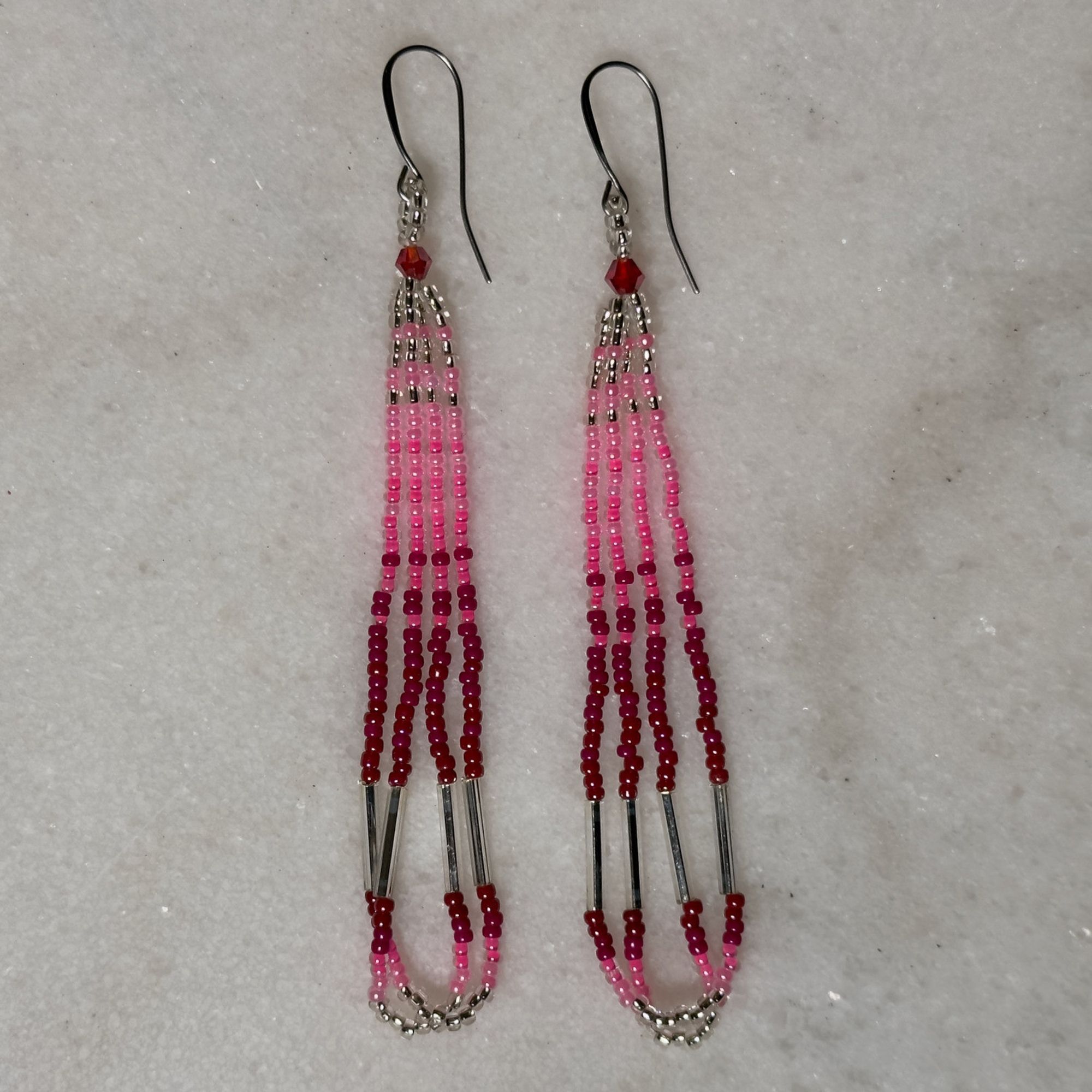 A pair of pink and silver beaded loop earrings on a marble background