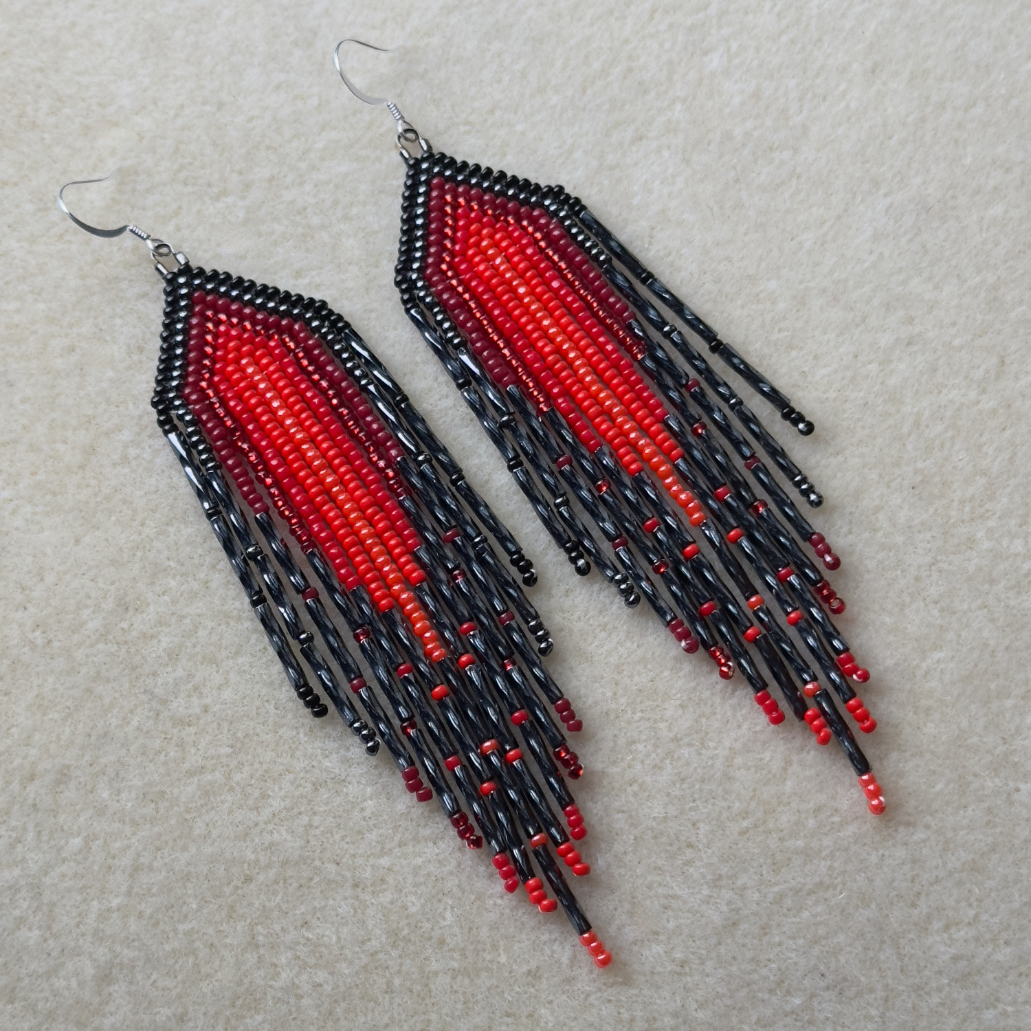 A pair of red and black beaded fringe earrings on a bead mat