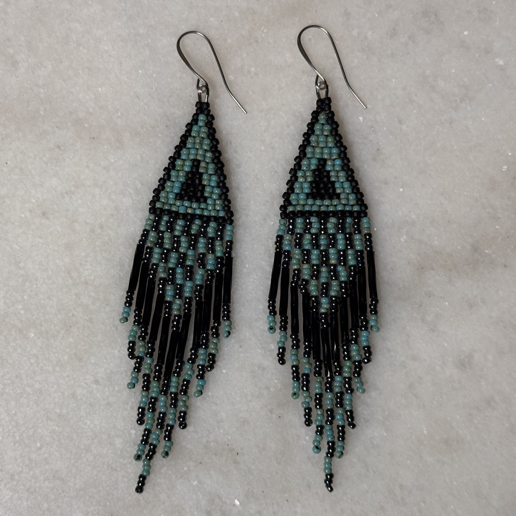 A pair of turquoise and black beaded fringe earrings on a marble background