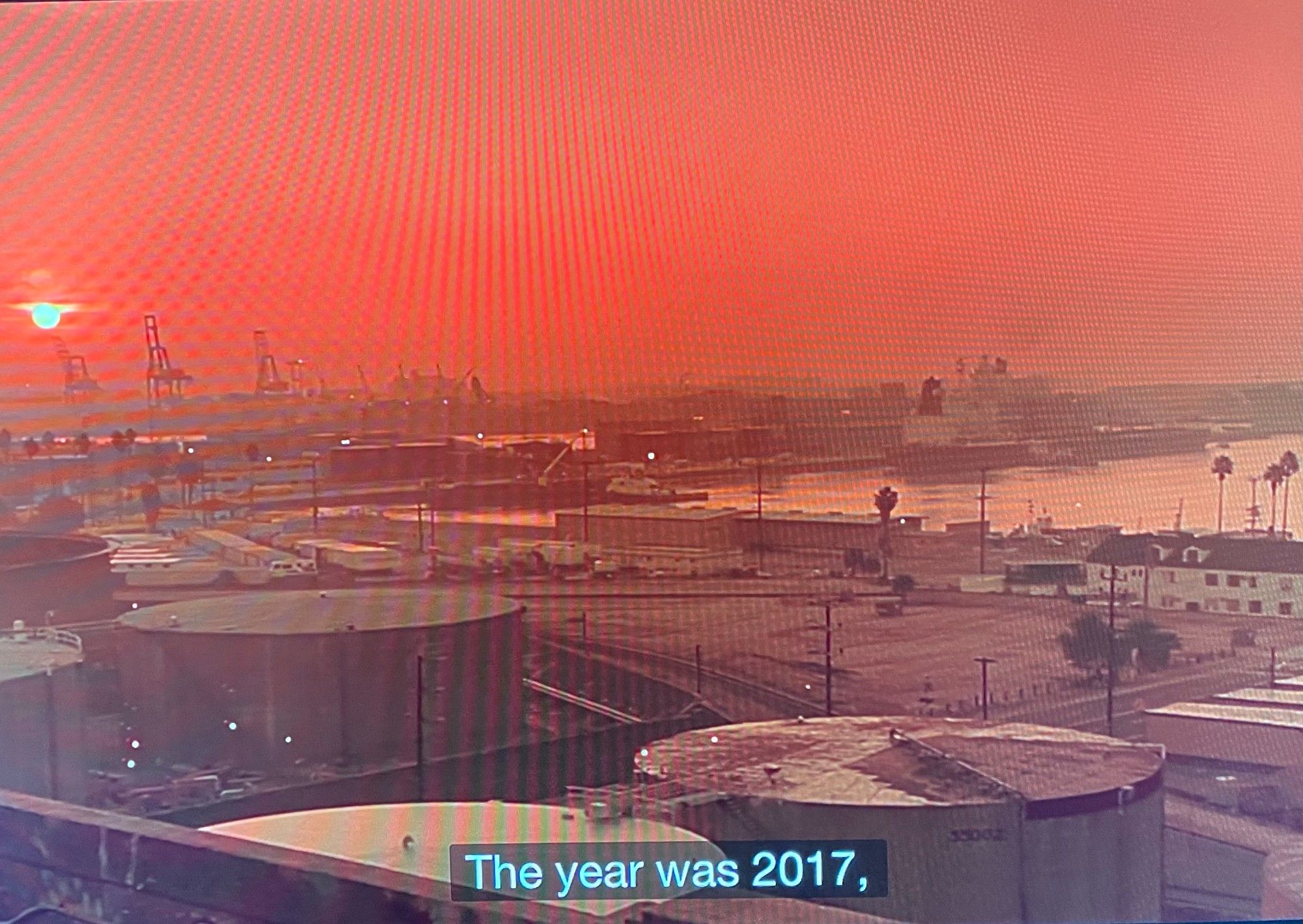 Industrial wasteland in a dystopian landscape at sunset under a smoky orange sky.