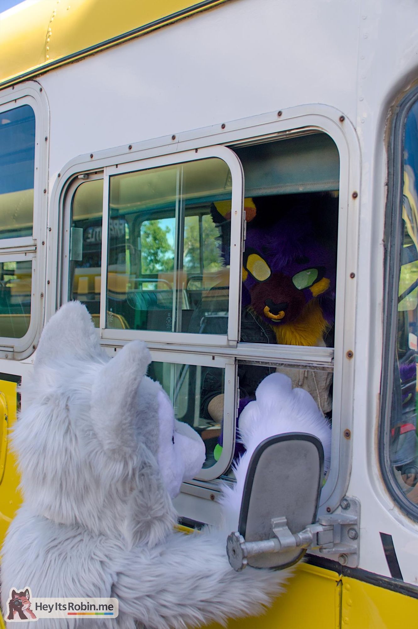 Casper, a cat fullsuit, stands at the open driver's window of a vintage bus, taking to Styx, a batdog partial fursuit, who sits in the driver's seat leaning out the window.