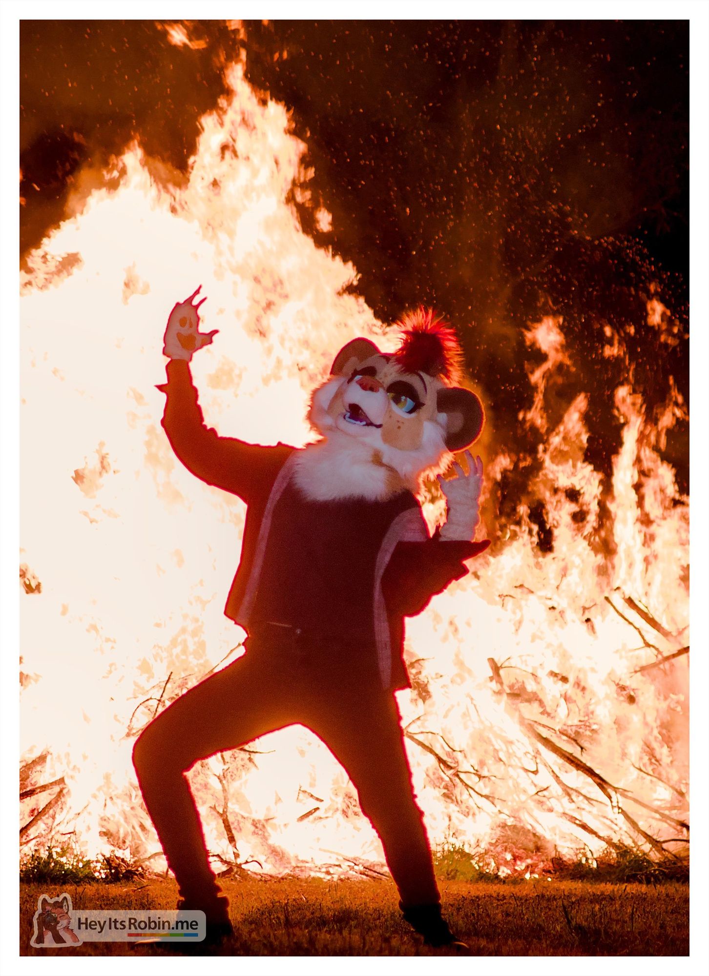 A photo of Sneaky, a lioness partial fursuit, standing in front of a bonfire that towers over her as she cackles maniacally, hands thrust to the sky; the form of the fire mirrors her pose, giving the illusion that she is controlling the fire with powers unknown.