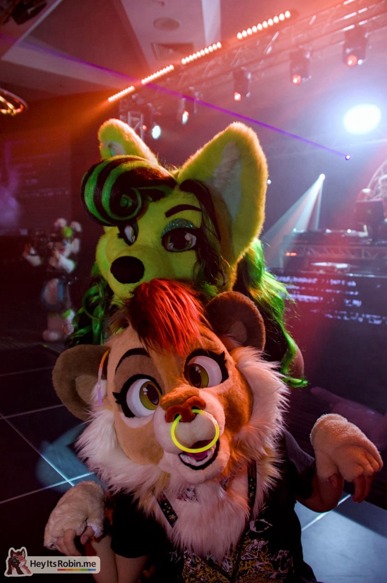 Sneaky, a look fursuit, and toxi, a dog fursuit, stand together on the dance floor at a rave, surrounded by laser lights, looking at the camera. Sneaky has a glow stick nose ring.