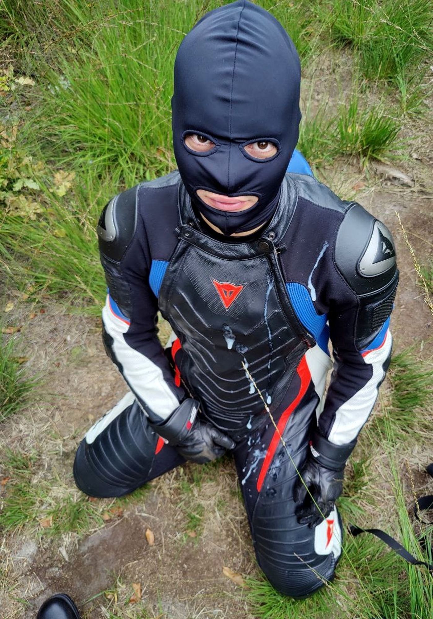 A leather-masked biker kneeling on grass covered in cum.