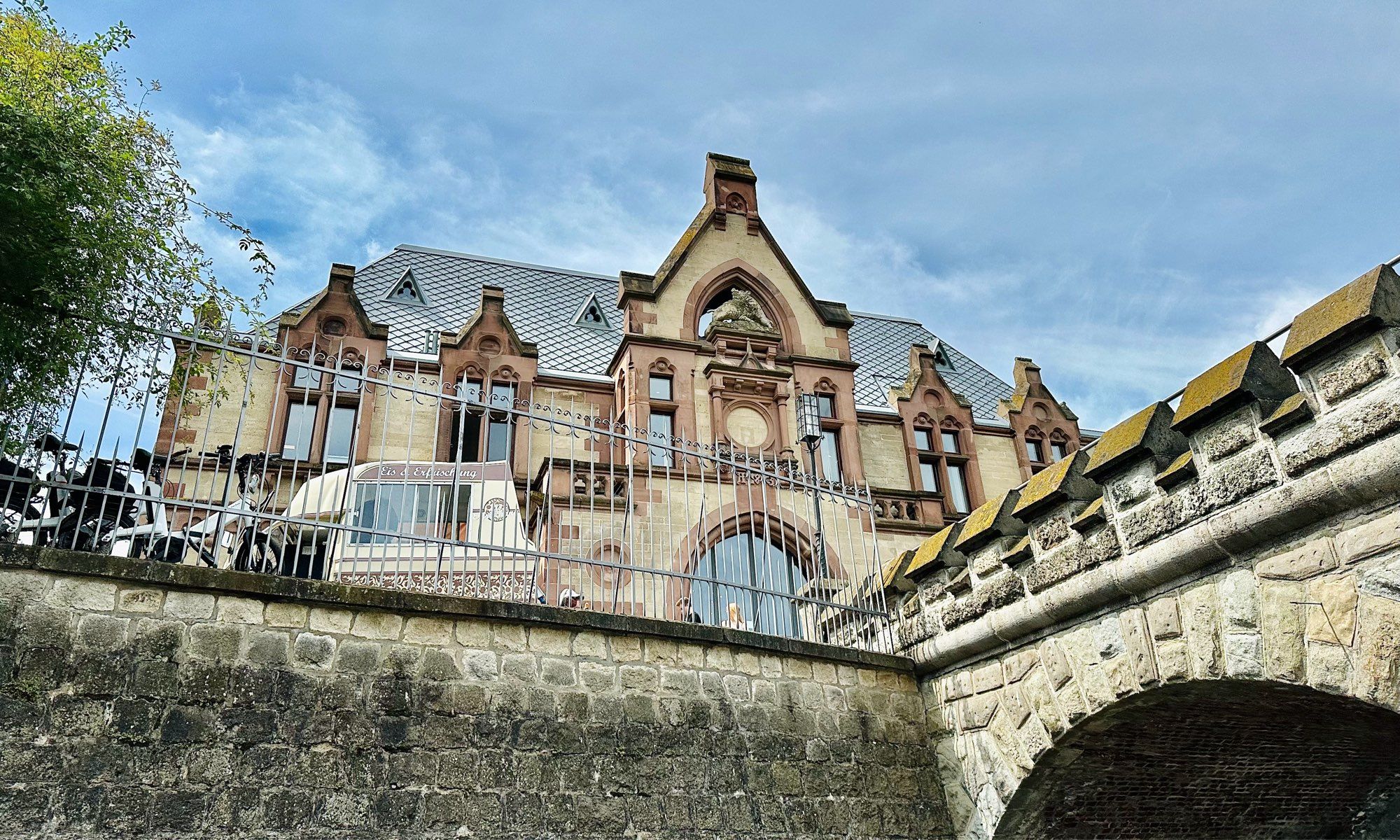 Die Vorburg des Schloss Drachenfels. Rechts im Bild der halbe Bogen einer Steinbrücke. Vor der Vorburg ist ein Eiswagen zu sehen.