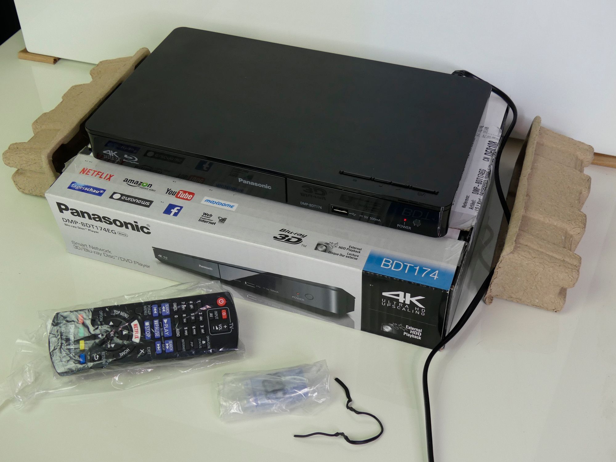 Ein gebrauchter PANASONIC Blu-Ray-Player, UHD mit 4K Upscaling, mit Fernbedienung, steht auf seinem Originalkarton und sieht echt gut erhalten aus. Er wird aktuell im Ebay-Shop von APLAWIA e. V.  deutschlandweit angeboten. VDE-geprüfte Qualität.