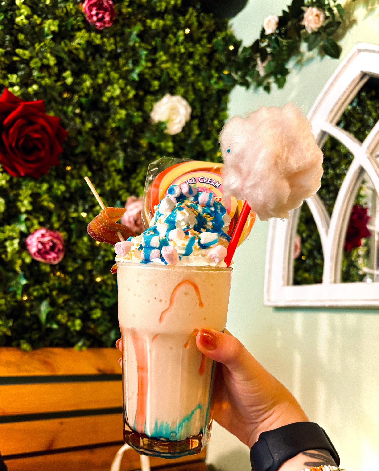 a vanilla milkshake with cream, marshmallow, lollipop and candy floss on top