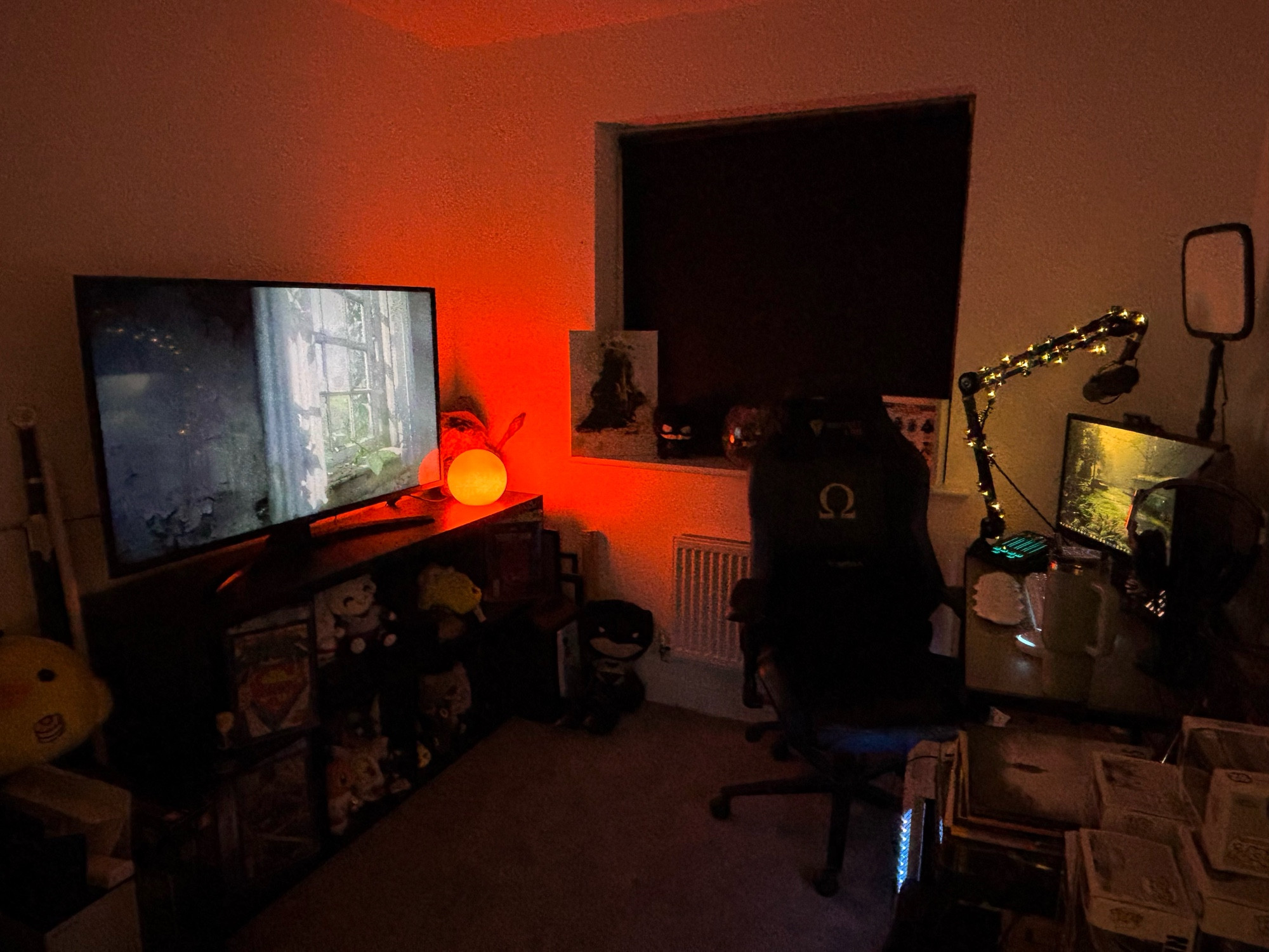 noskus gaming room with a kallax and a tv with her computer set up. the light is orange and is dimly lighting the room 