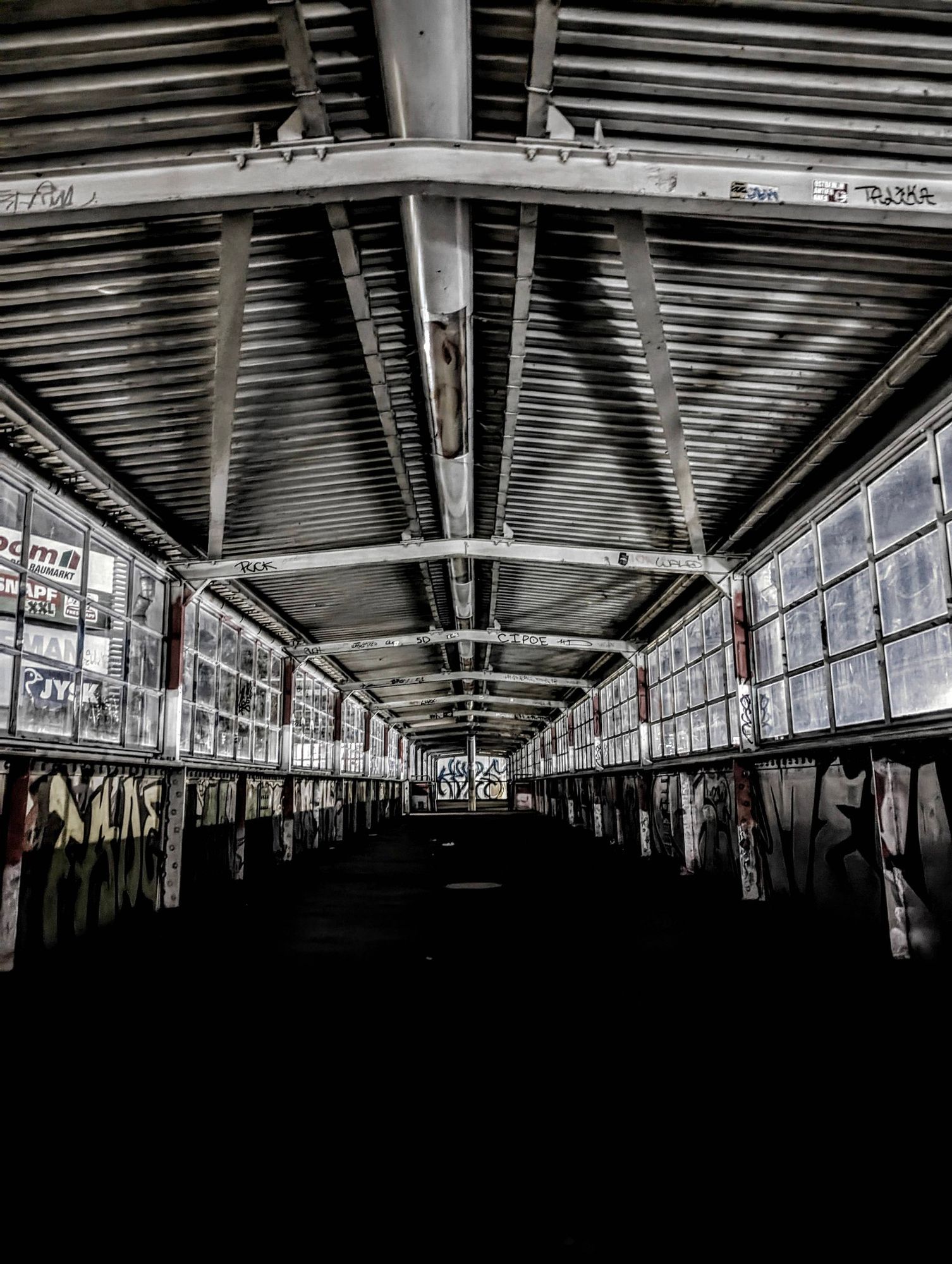 Ein geschlossen überdachter Fußgängerübergang am Bahnhof Storkower Straße.
Ein Alu - Blechdach, Stahlträger-Konstruktion, Fensterfronten aus Glas, darunter geschlossen und voller Graffiti.