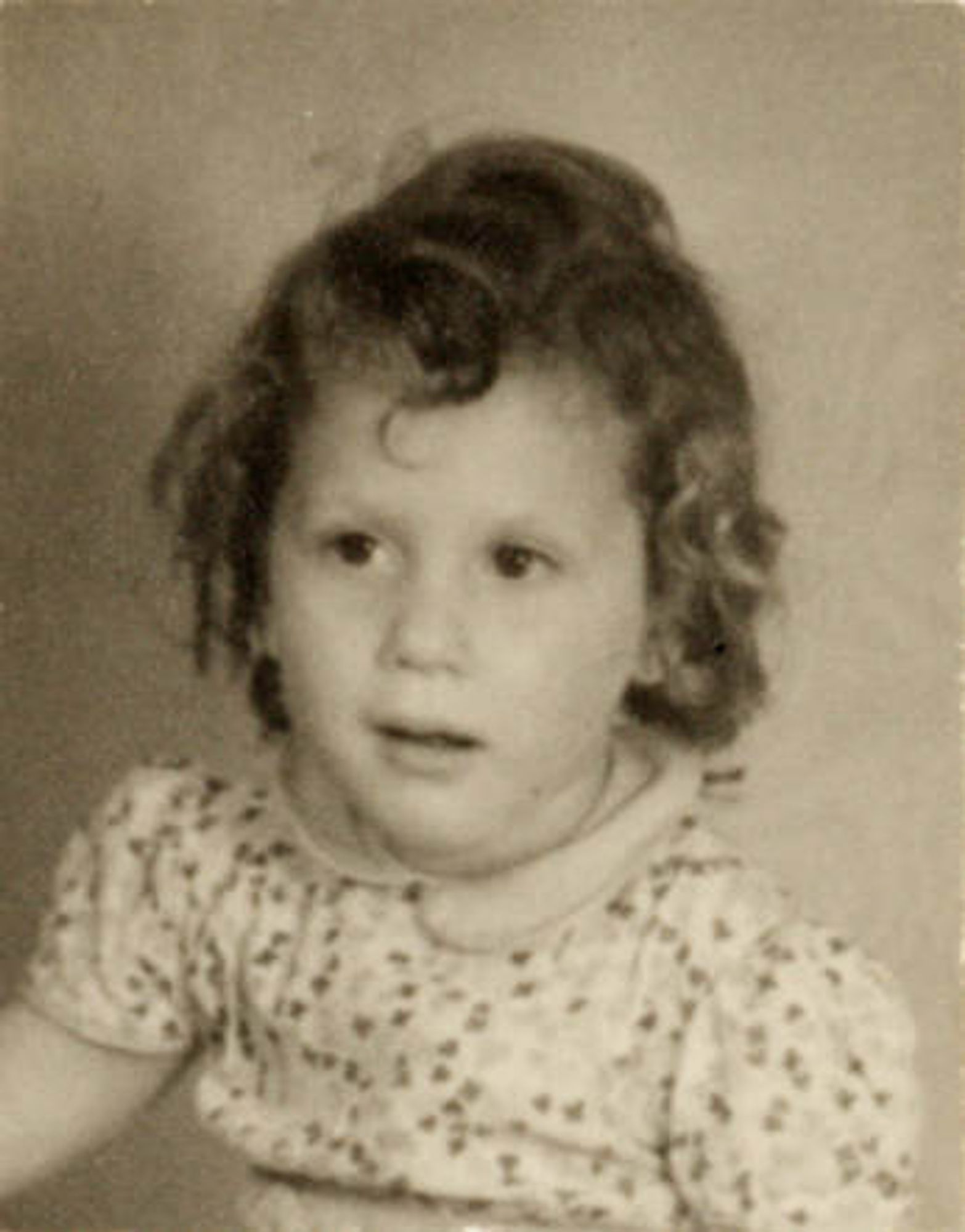 Vintage black and white photograph of a young girl with curly hair, wearing a patterned shirt.