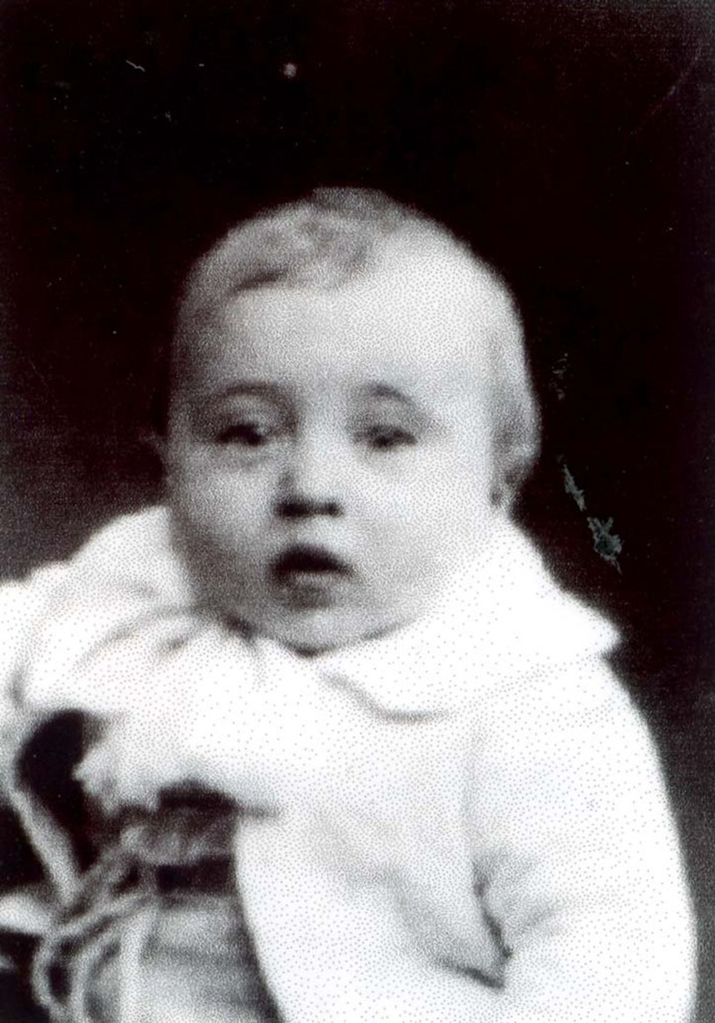 A historical black and white photograph of a baby wearing a light-colored outfit.