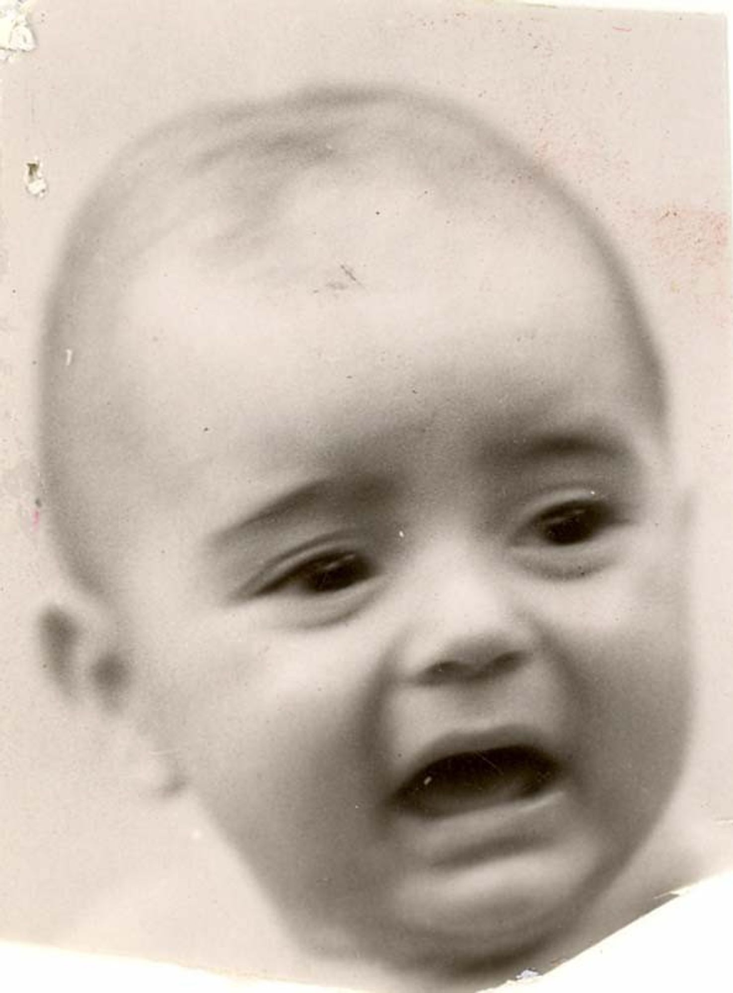 A black-and-white photograph of a baby boy, appearing to be crying or upset. The image is somewhat blurred, but the facial features of the child, including wide eyes and an open mouth, are visible. The baby has a small amount of hair and seems quite young.