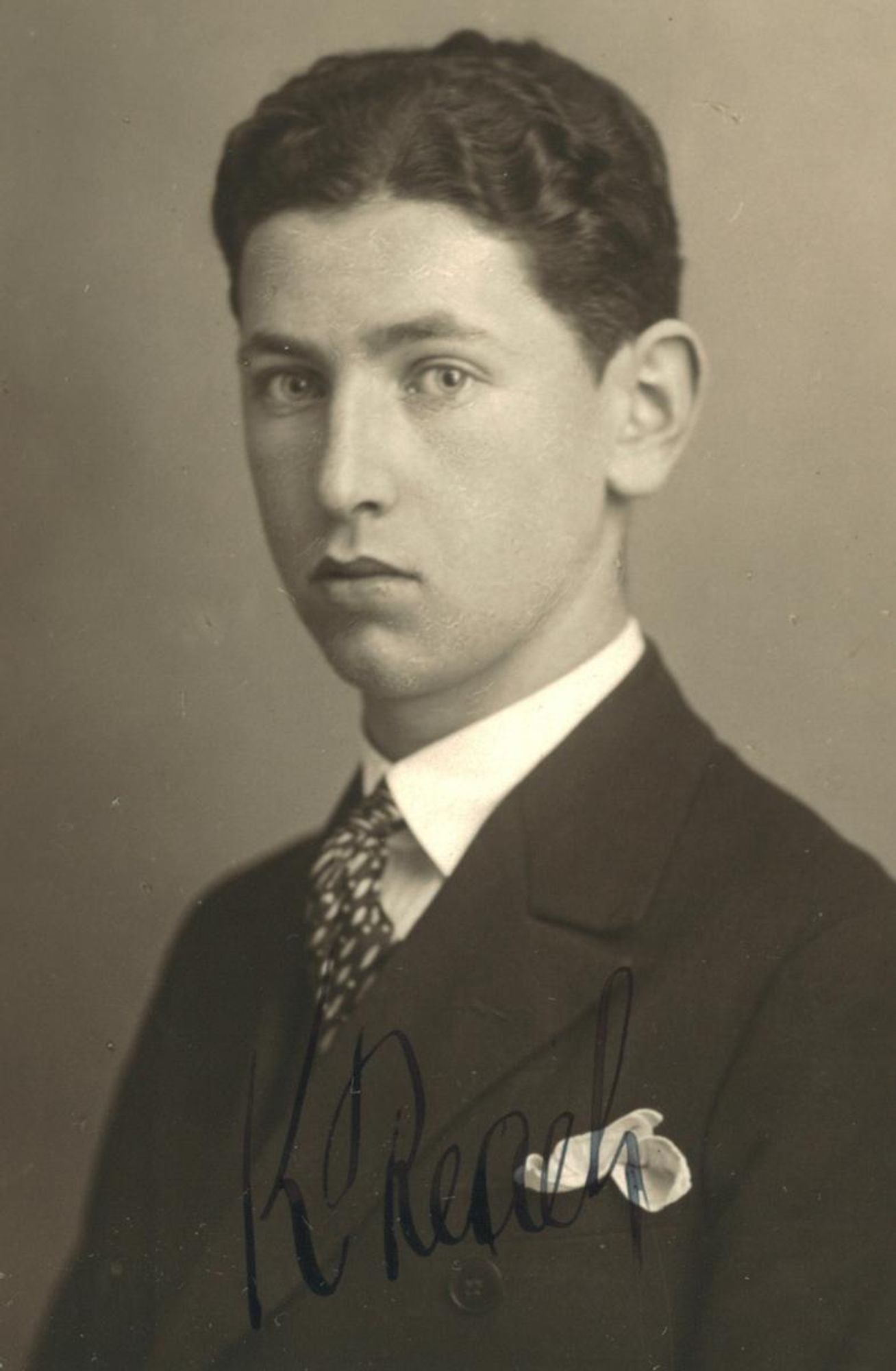 Vintage black-and-white portrait of a man in a suit with a patterned tie. The photograph features an autograph at the bottom.