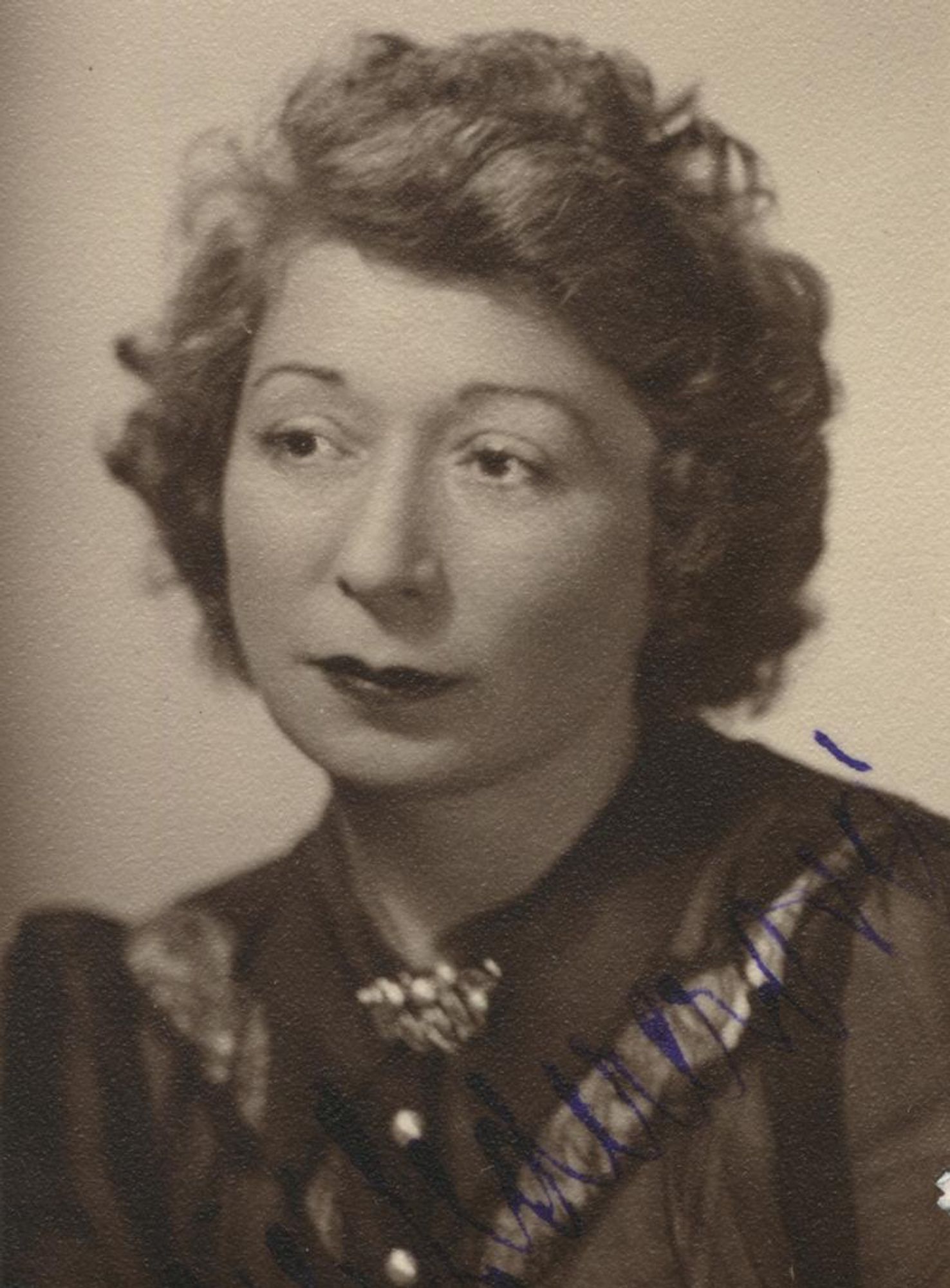 Vintage black and white portrait of a woman, with thoughtful expression, featuring curly hair and a dark blouse adorned with a necklace.