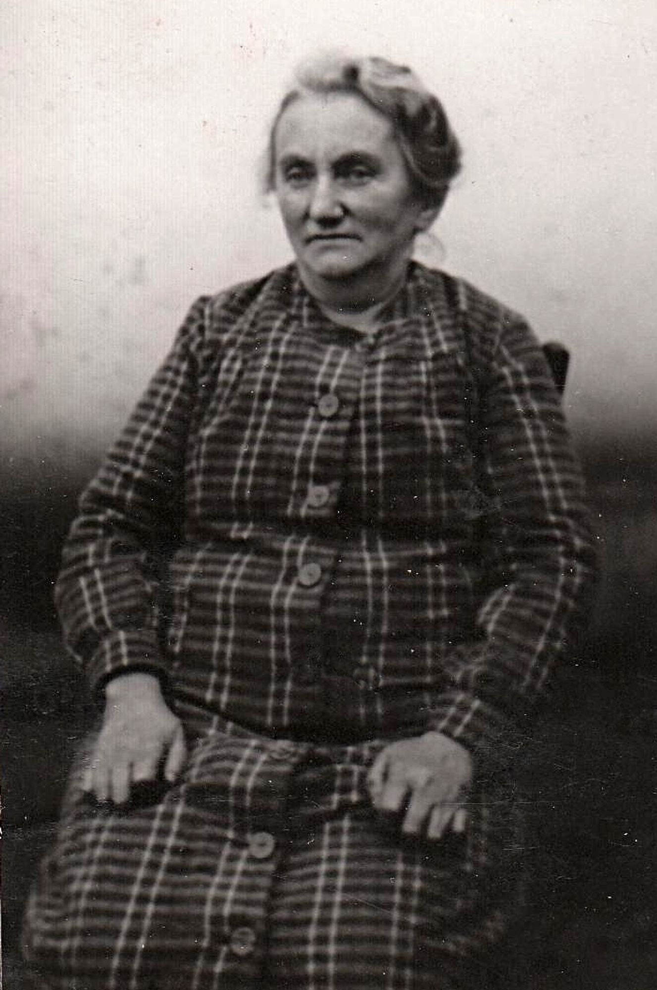 Vintage black-and-white photo of a seated woman in a plaid dress, with a calm expression.