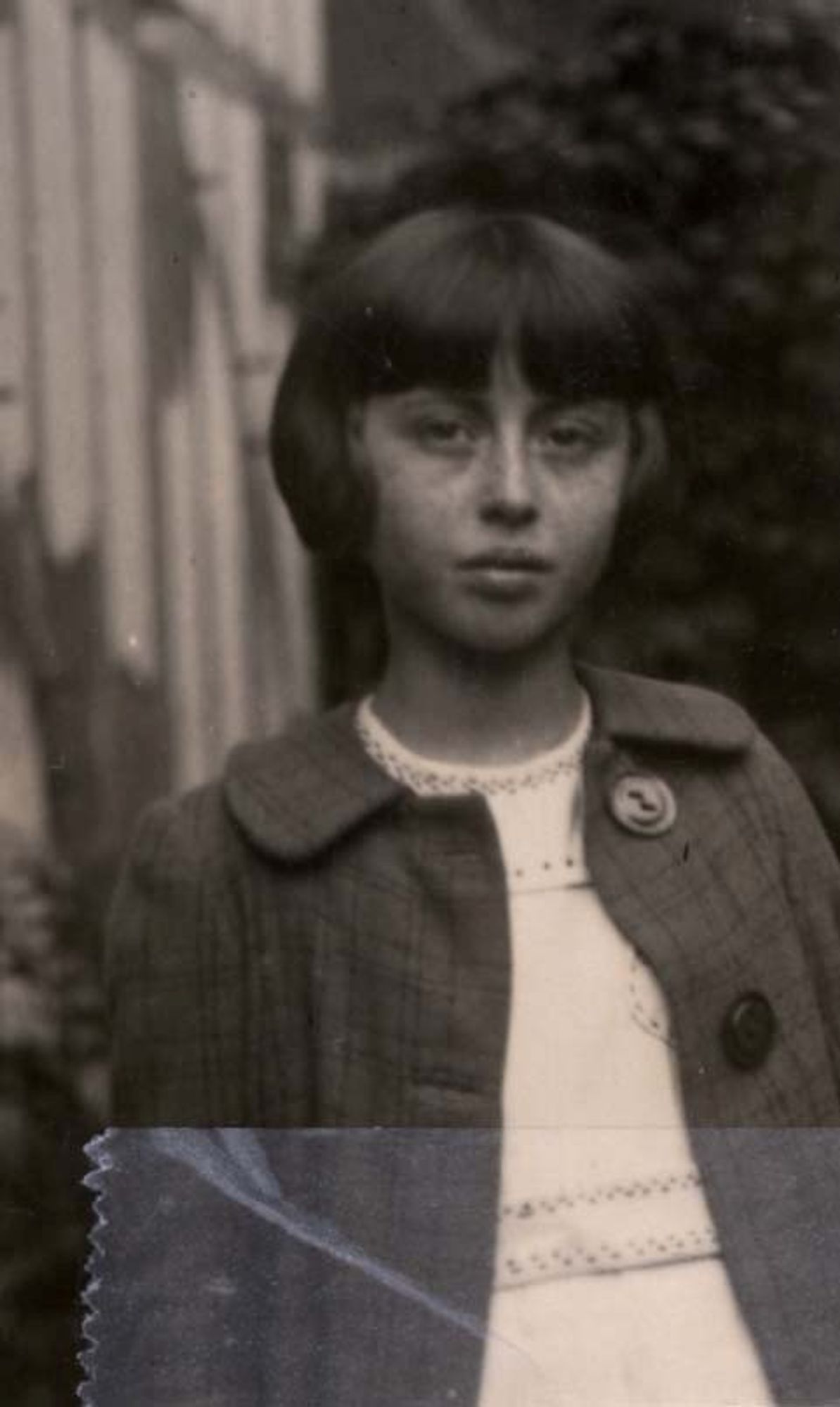 Vintage black and white photo of a young girl with a serious expression, wearing a coat with a button and a collared shirt.