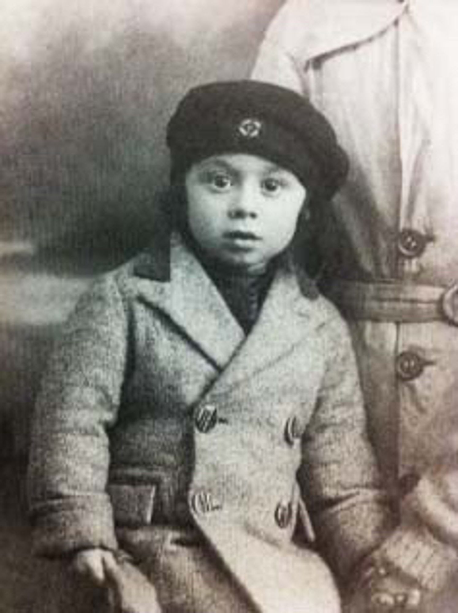 Vintage black and white photo of a young boy wearing a beret and a double-breasted coat.