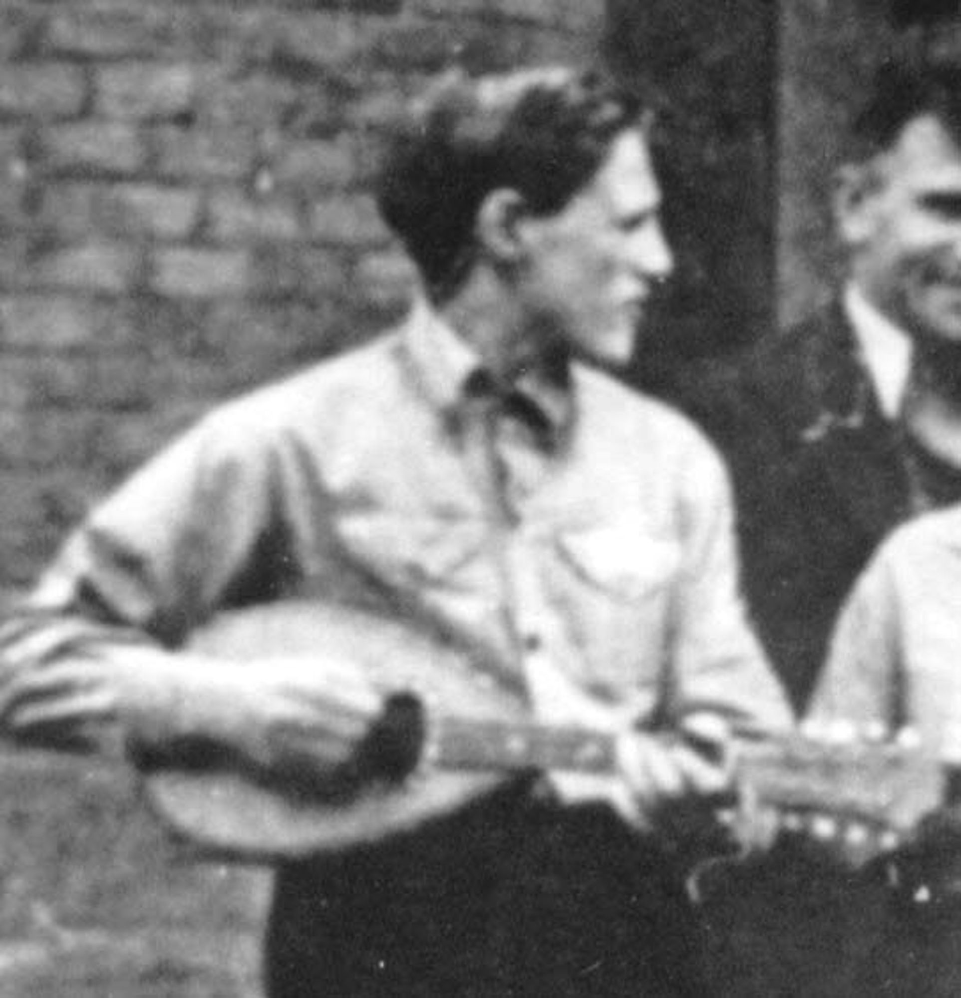 A man smiling while holding a guitar, standing next to an unidentified person.