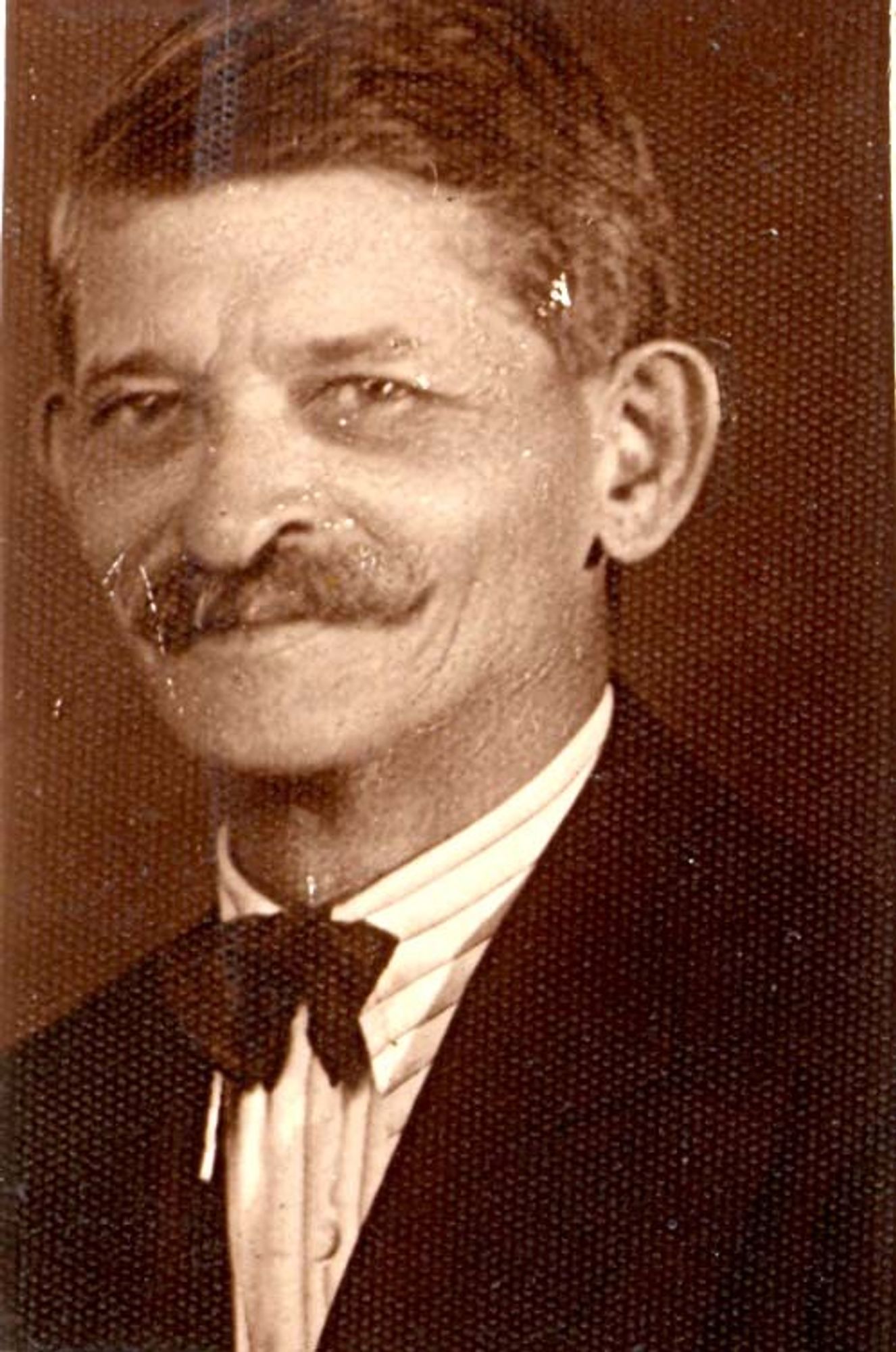 Vintage sepia-toned portrait of a man with a prominent mustache wearing a bow tie.