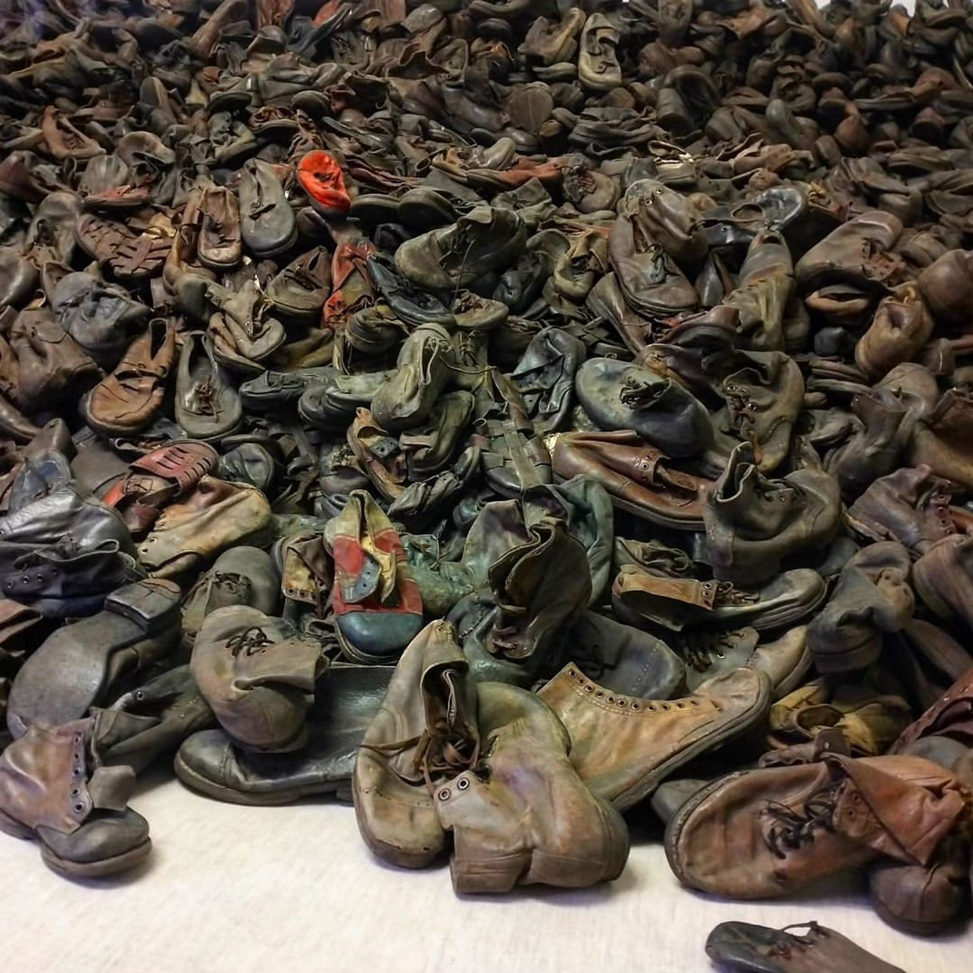 A large pile of worn, old children's shoes, with some scattered in the foreground. Fragment of the exhibition of the Auschwitz Memorial