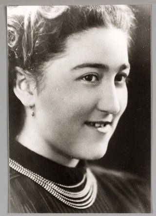 Black and white portrait a woman, smiling and dressed in a dark outfit with a multi-strand necklace.