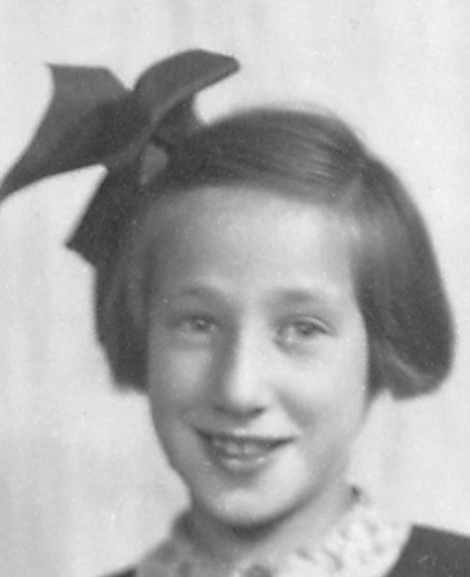 A vintage black and white portrait of a girl smiling, wearing a bow in short hair.