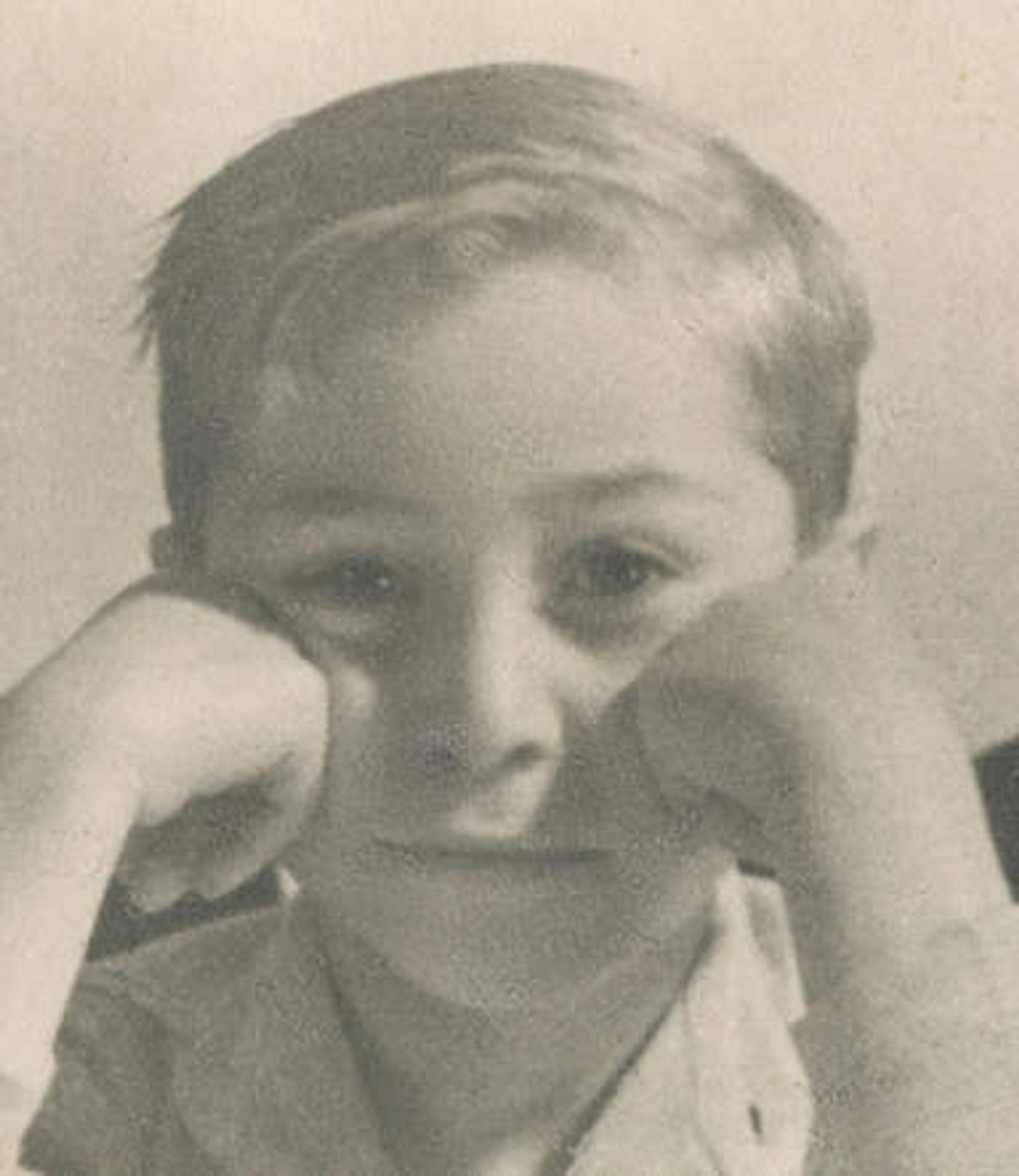 Vintage black and white photo of a young boy resting their chin on their hands, looking thoughtful.