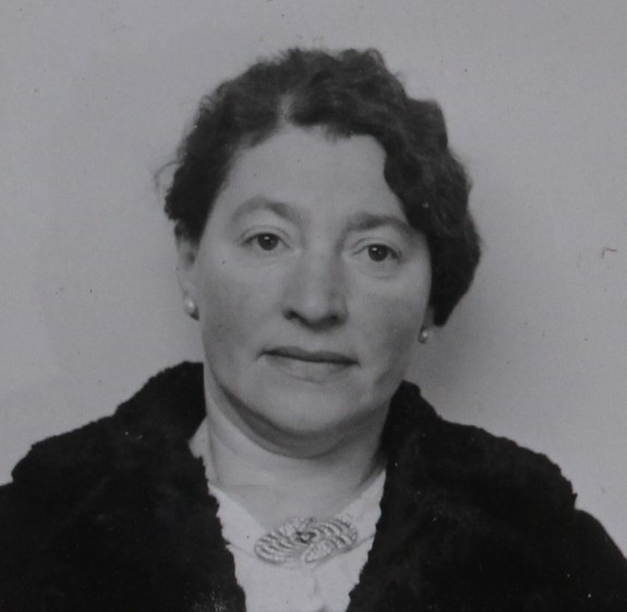 Black and white portrait of a woman with a confident expression, wearing a dark coat with a fur collar and a decorative brooch.