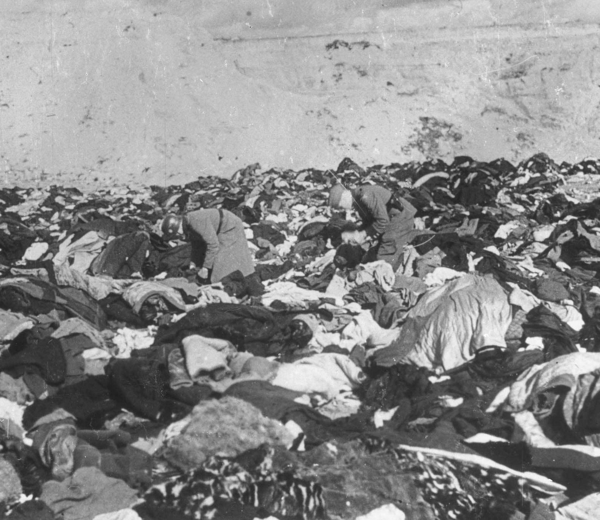 Photograph of German soldiers searching through a large pile of clothing and belongings of victims in Babi Yar ravine.