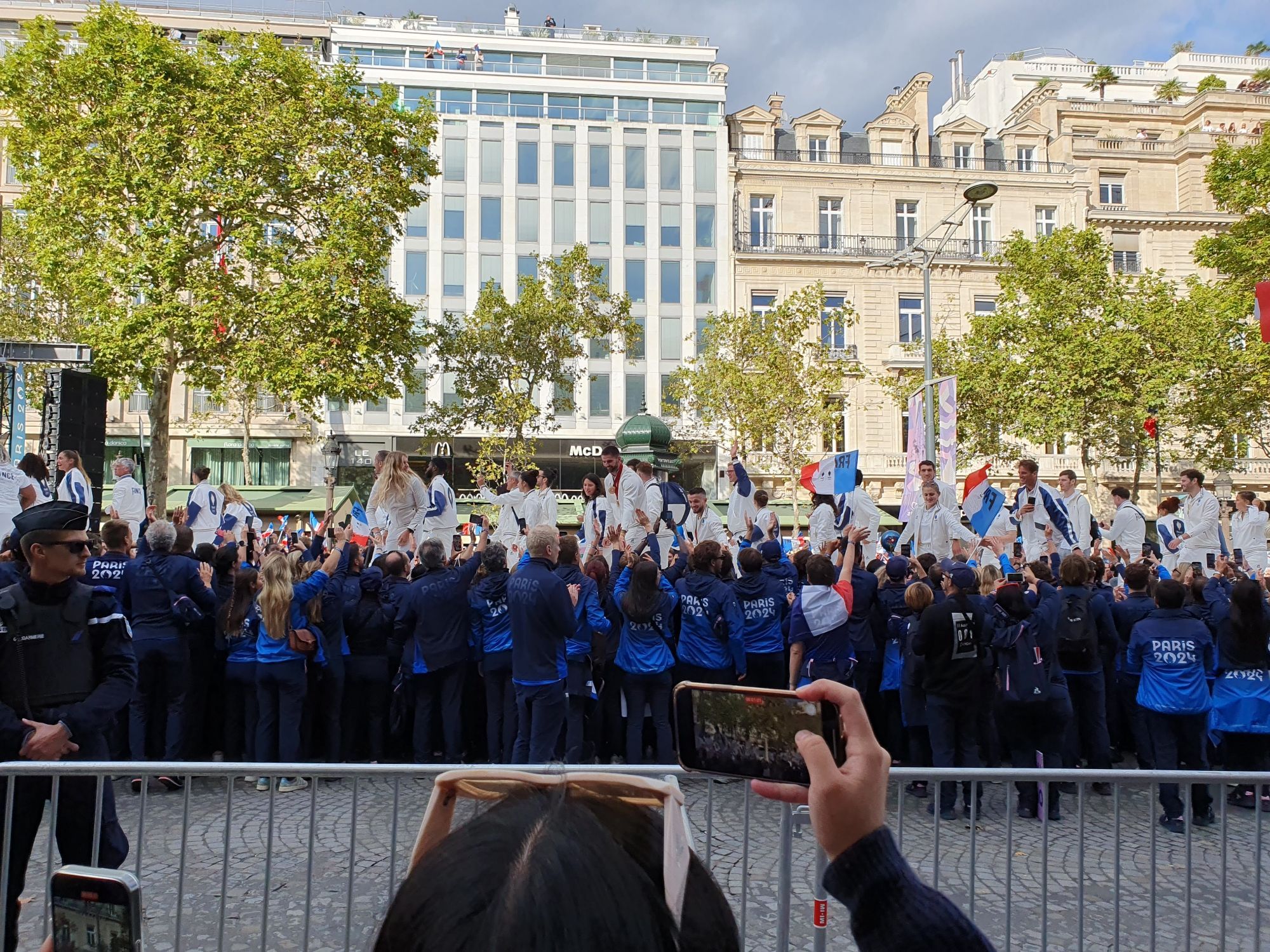 French Olympic and Paralympic champions on a catwalk on the Champs Elysées with Paris 2024 staff dressed in their blue uniforms on the sides, lots of French flags