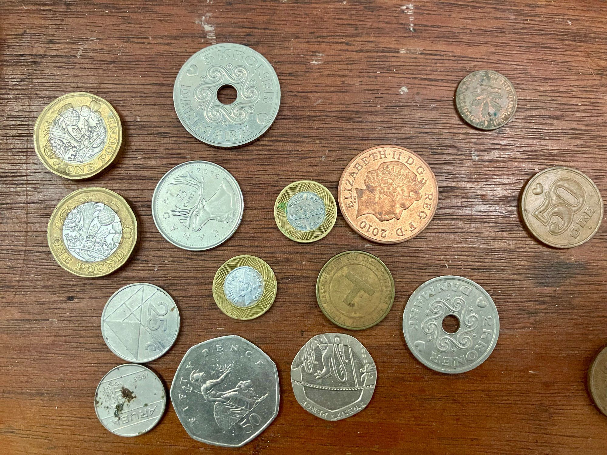 Photo of a variety of coins on a wood surface, some with holes in the middle, some two toned.